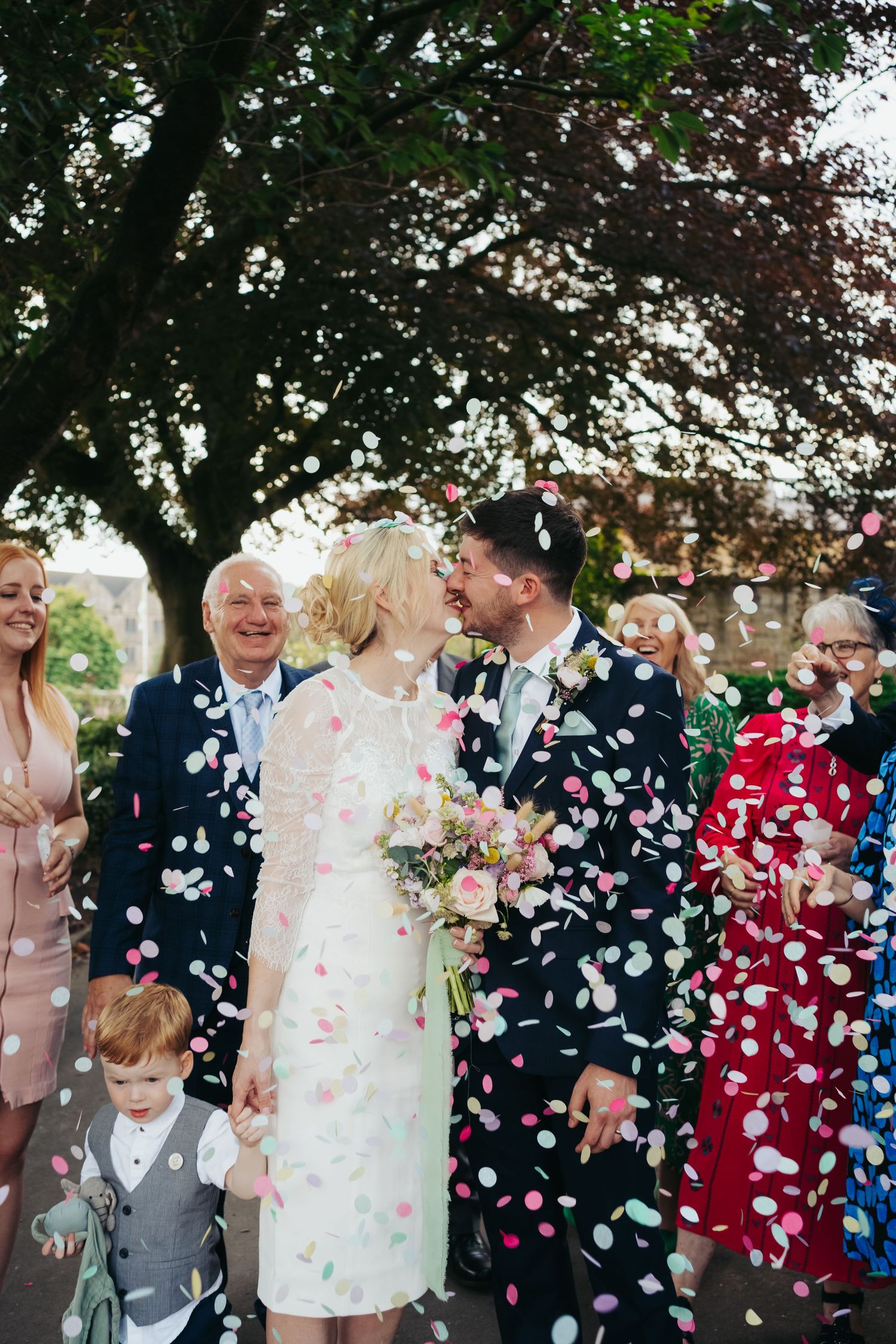 Family throw confetti onto bride and groom couple during small intimate elopement with their children. bride wears modern short dress