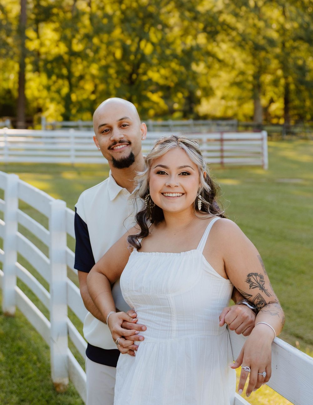 A sunny outdoor photoshoot by a white picket fence in a grassy field.