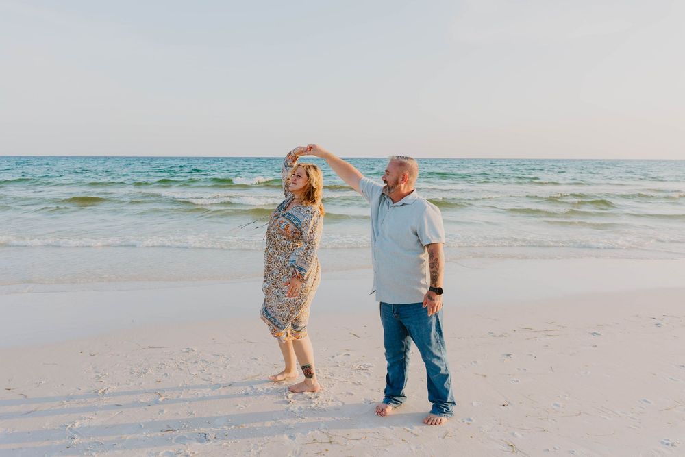 Two people stroll together on an empty beach with waves and ocean in the background.
