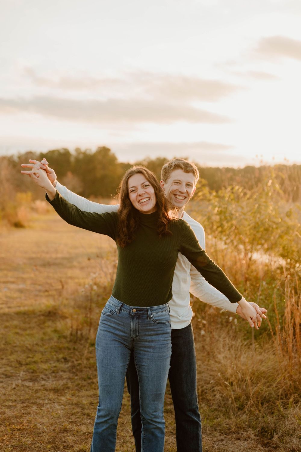 Playful couple spreading arms like wings in warm evening light.