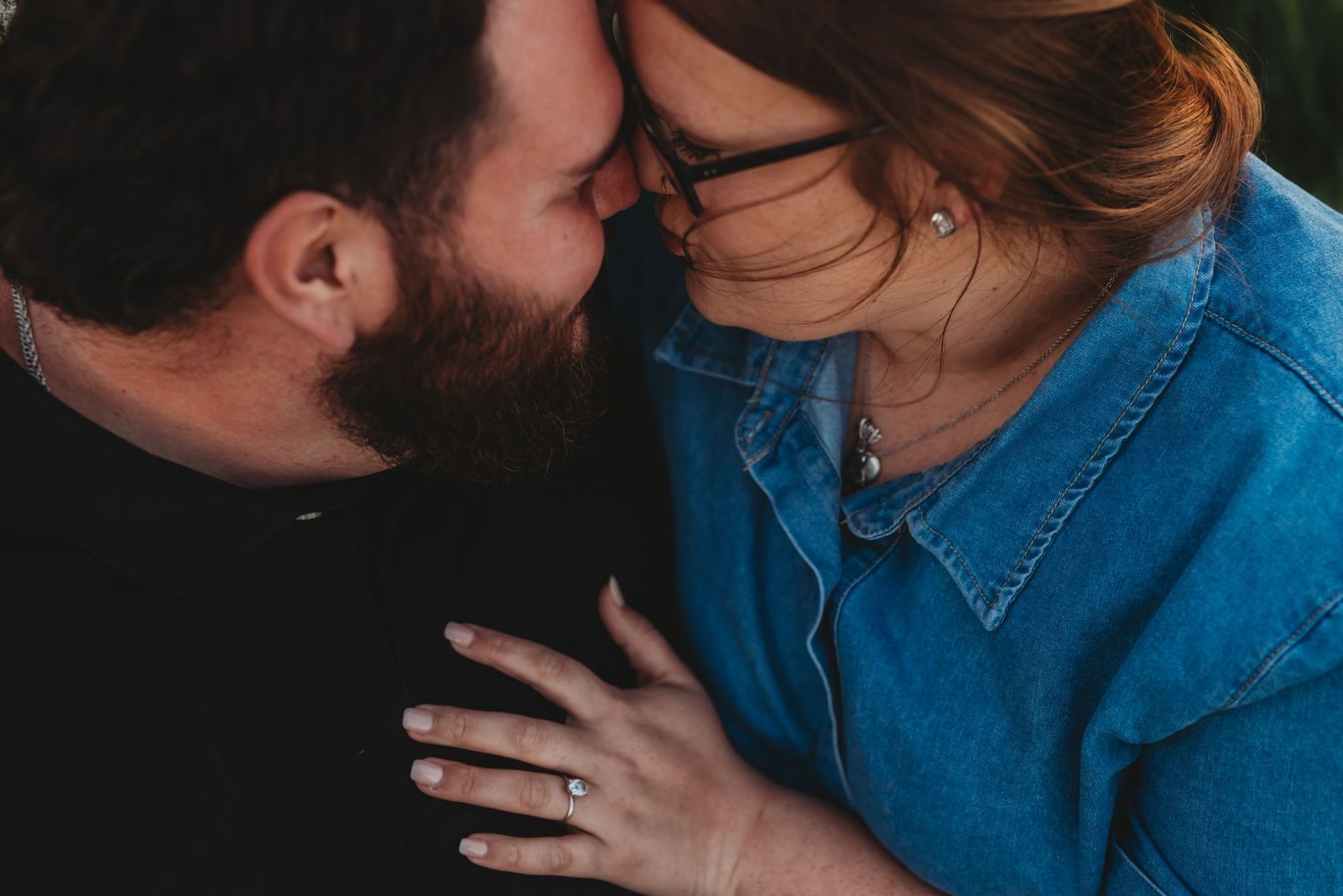 Close up intimate moment between two people with one wearing a denim shirt, captured in soft lighting.