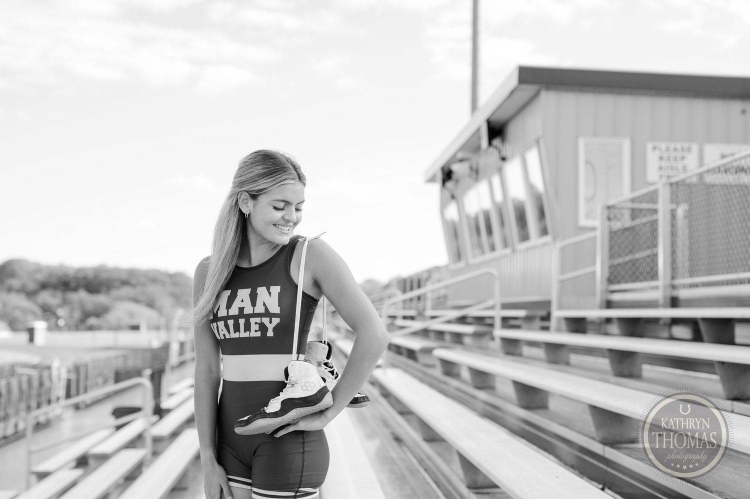 Black and white photo of an athlete in a Manchester Valley uniform sitting on stadium bleachers.