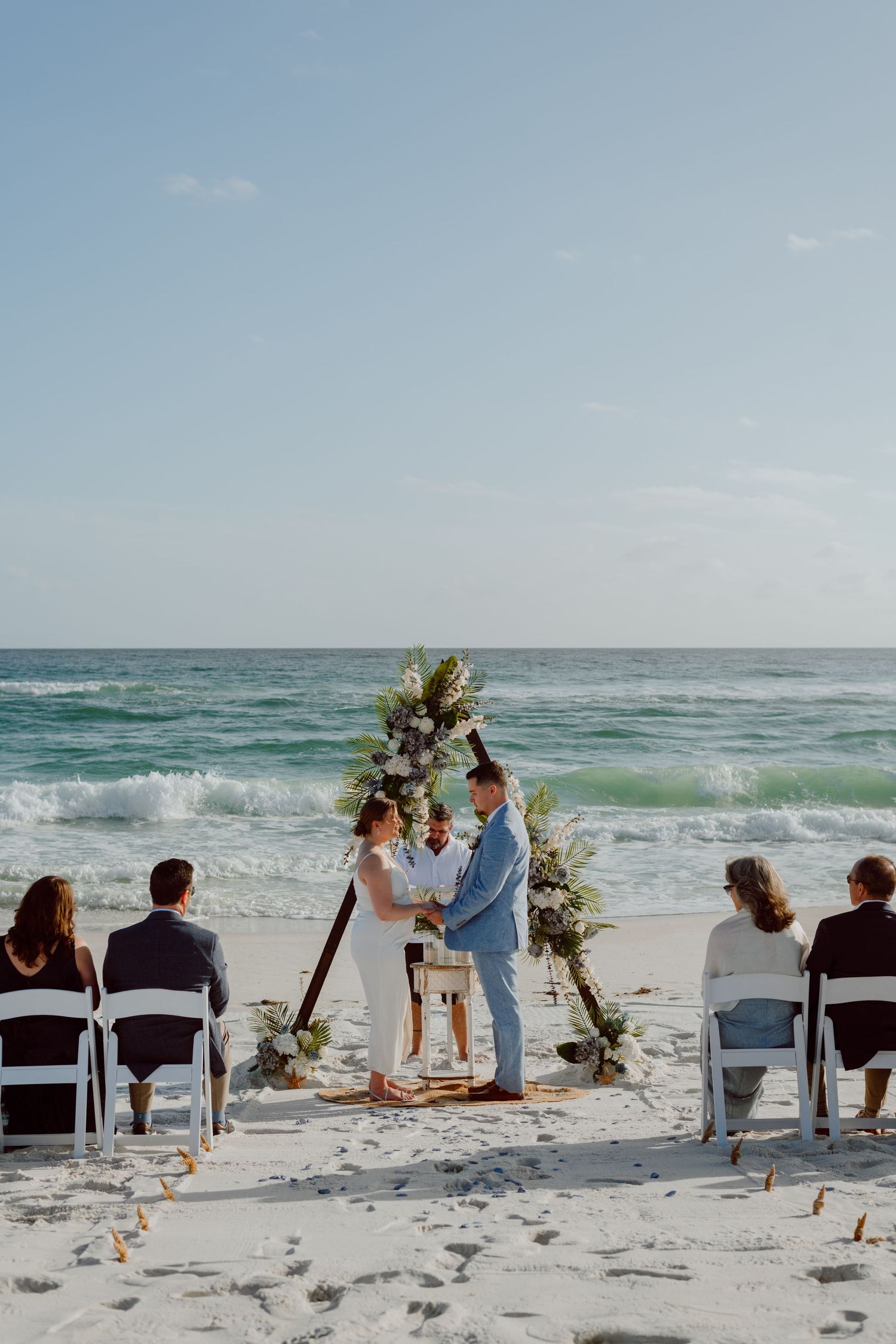 Intimate beach wedding ceremony with floral arch and ocean backdrop.