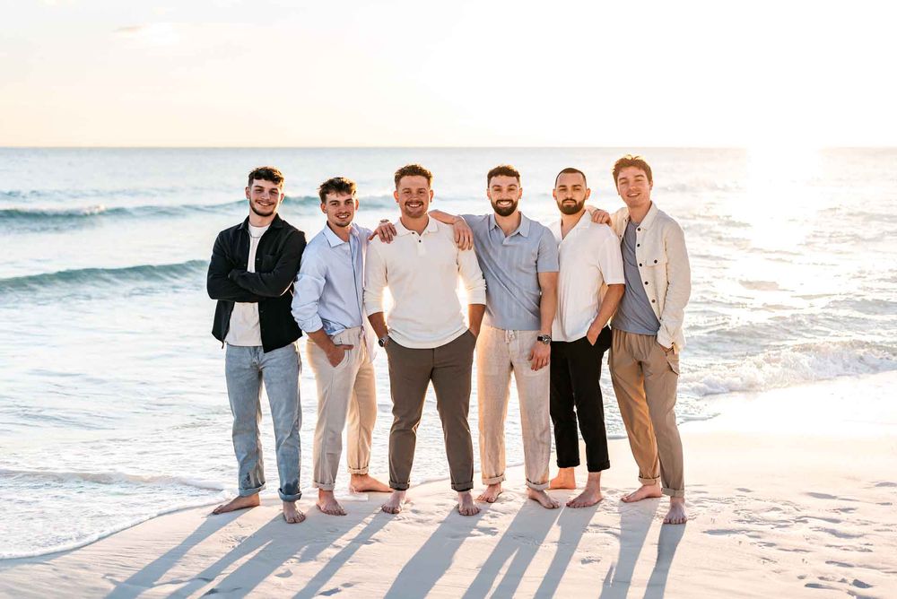 Group portrait of friends and family on a beach at sunset wearing coordinated neutral tones.