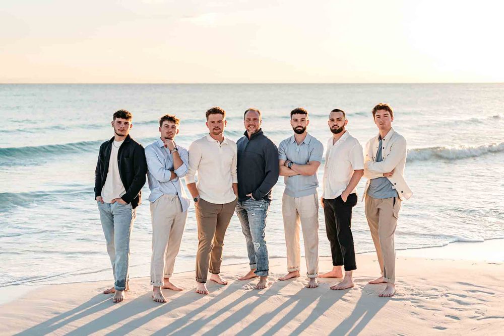 Line of people posing together on beach in casual neutral outfits during golden hour.