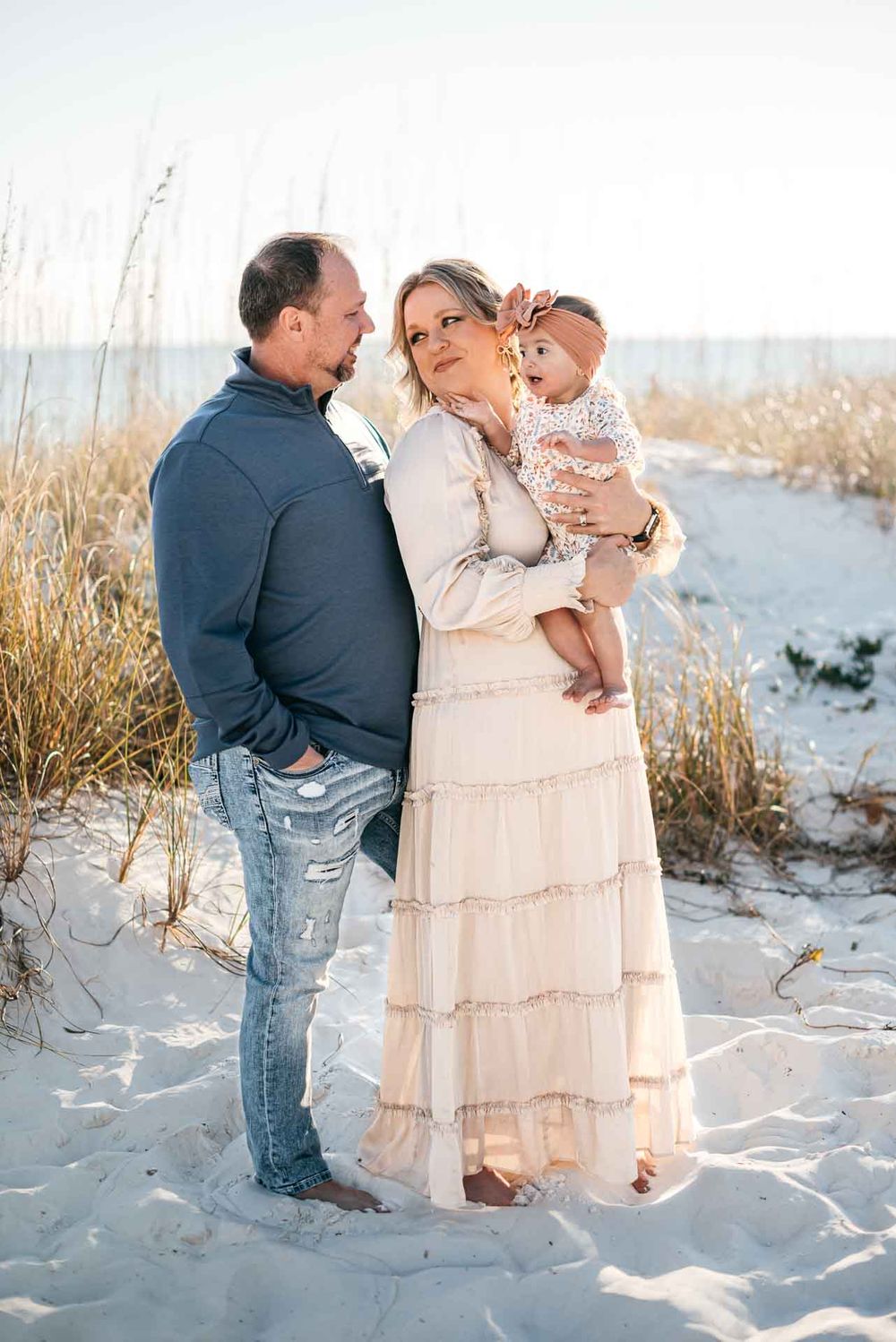 A family plays together on a white sandy beach with sea oats in the background.