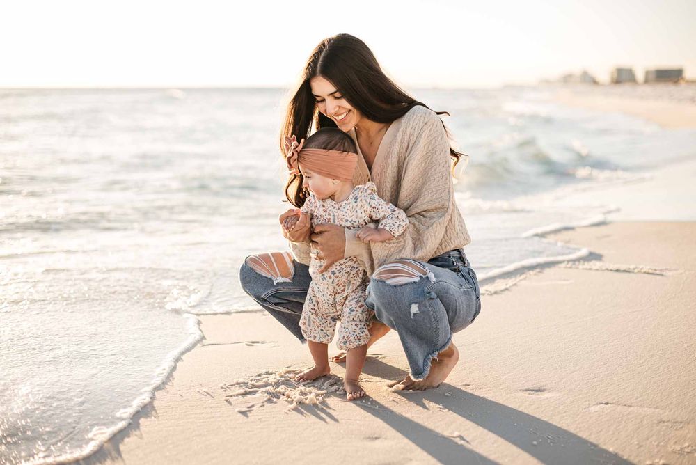 Parent and child playing in the sand at the beach during golden hour.