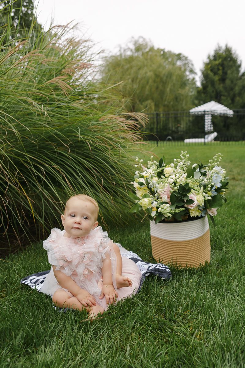 Birthday girl sitting on the grass with colorful florals next to her, captured by NYC family photographer Paula Ortiz