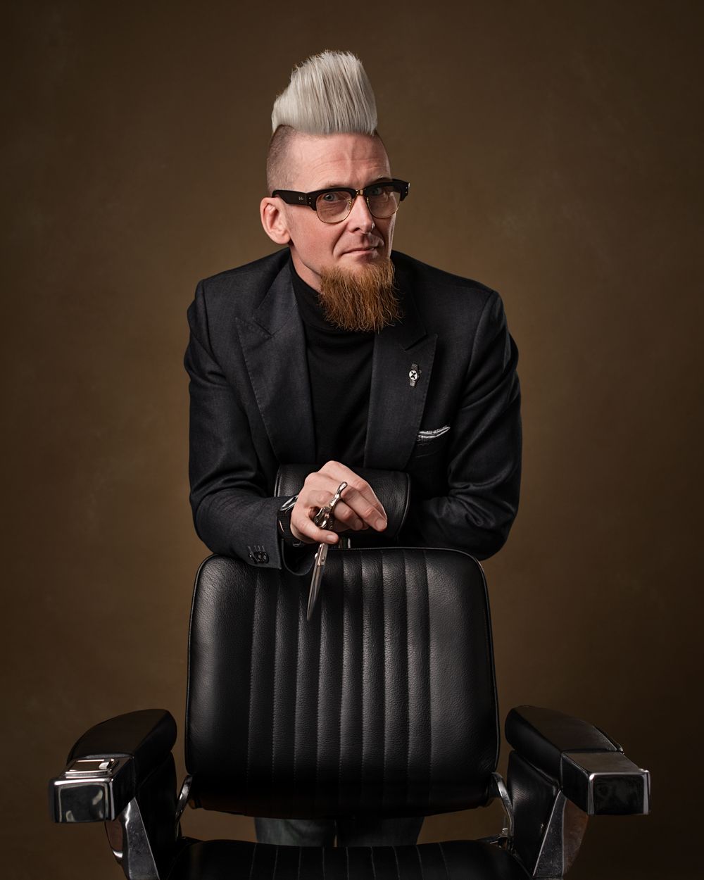 Jan Piet Joris en Corneel barbier met psycho quiff, leunend op een kappersstoel met een schaar. Professionele kappersportret fotoshoot.
