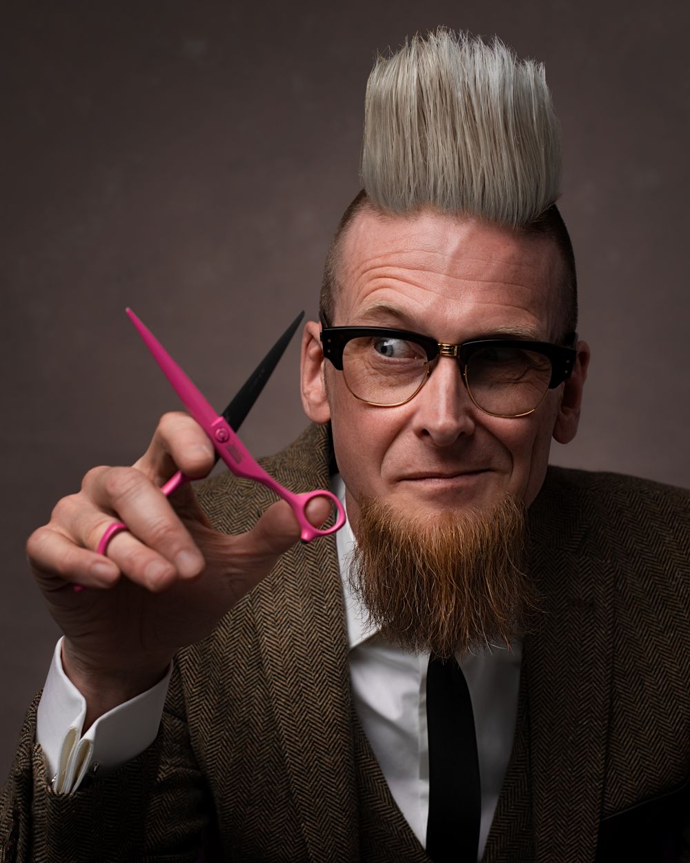 Kapper met retro look, bril en puntige baard, houdt een roze Mizutani schaar vast. Creatieve portretfotografie van een hairstylist.