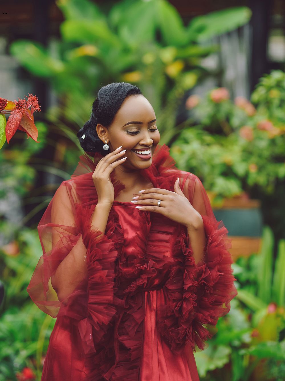 Person in flowing red tulle dress laughing in a garden setting.