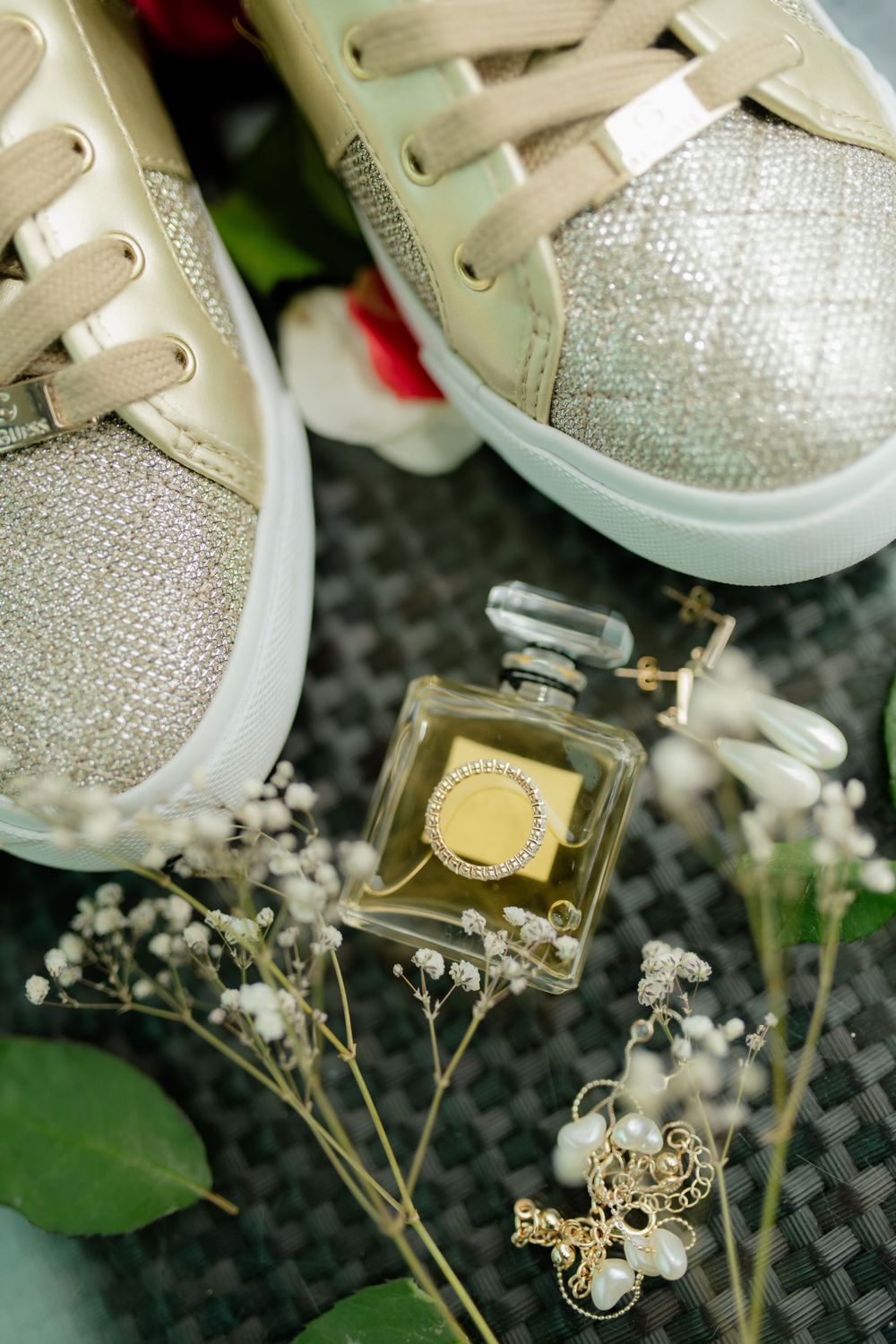 Glittery sneakers and a perfume bottle arranged with delicate baby's breath flowers on a dark surface.