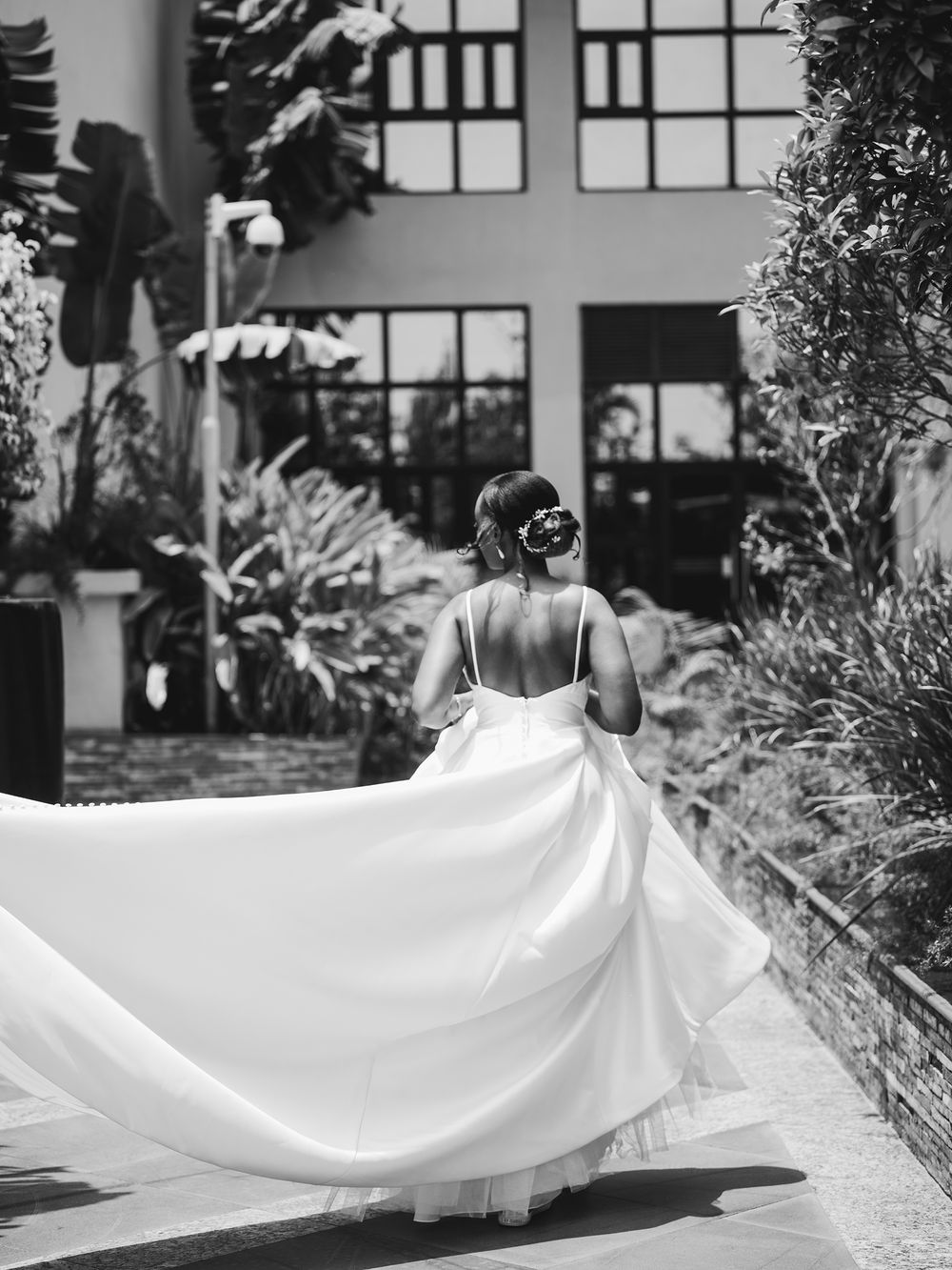 A stunning bride in a flowing white gown twirls on a garden pathway.