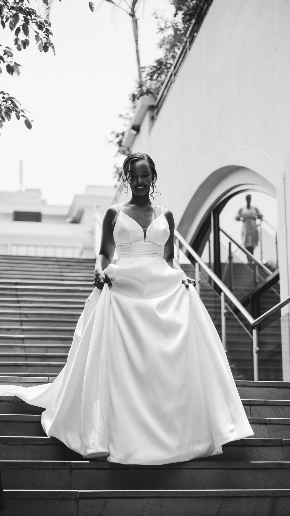 An elegant bride in a white ball gown poses gracefully on grand outdoor steps.