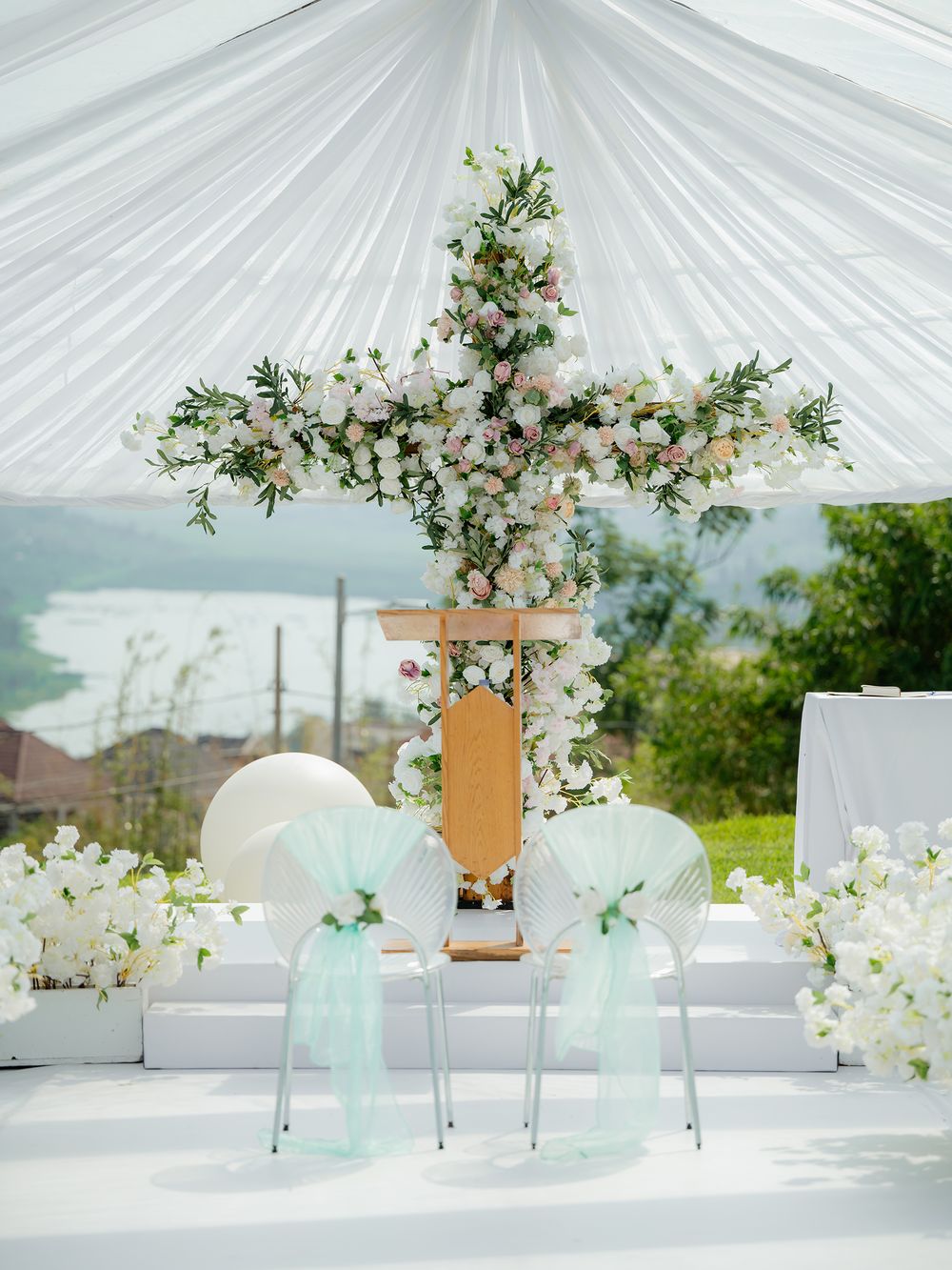 Romantic wedding ceremony setup with white floral cross arch and mint green accents.