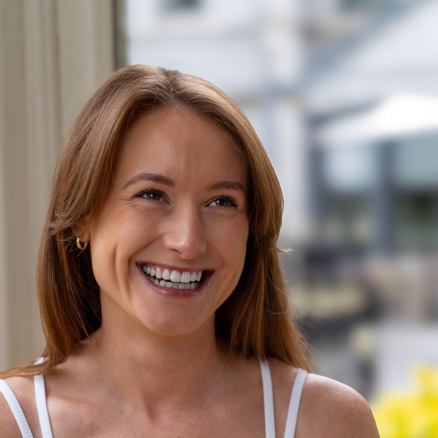 Portrait of woman in white tank top smiling warmly at camera.