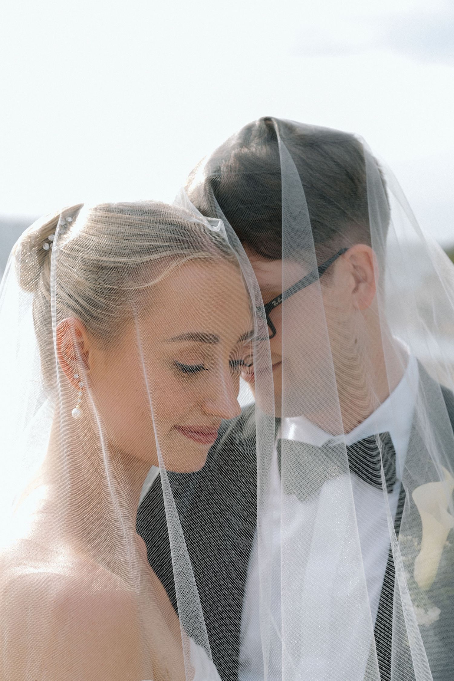 Intimate moment of a couple under wedding veil with soft natural lighting.
