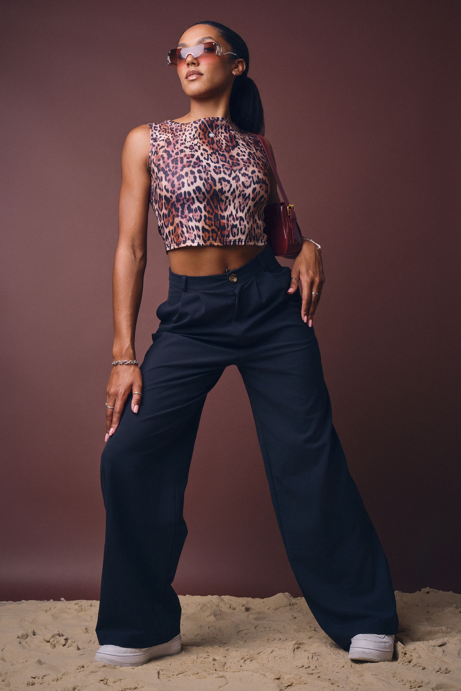 Female model in leopard print top and black trousers, posing with hands on hips against a solid background