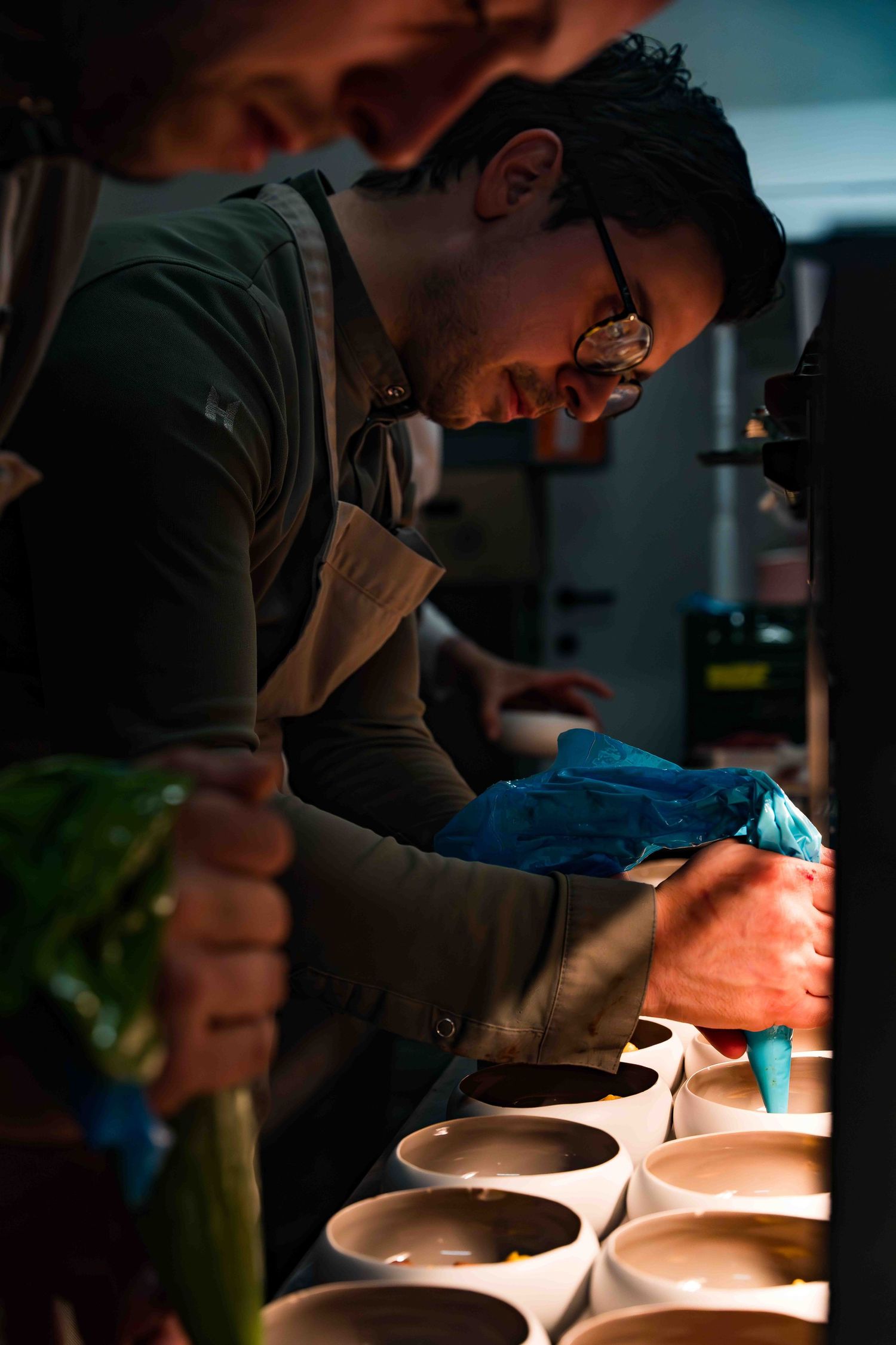 Chef carefully plating dishes in a dimly lit professional kitchen.