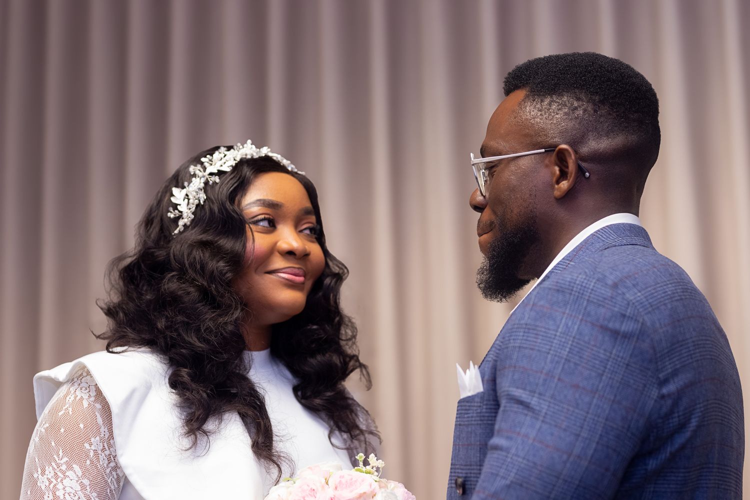 Wedding couple sharing intimate moment with bride in lace dress and groom in blue suit.