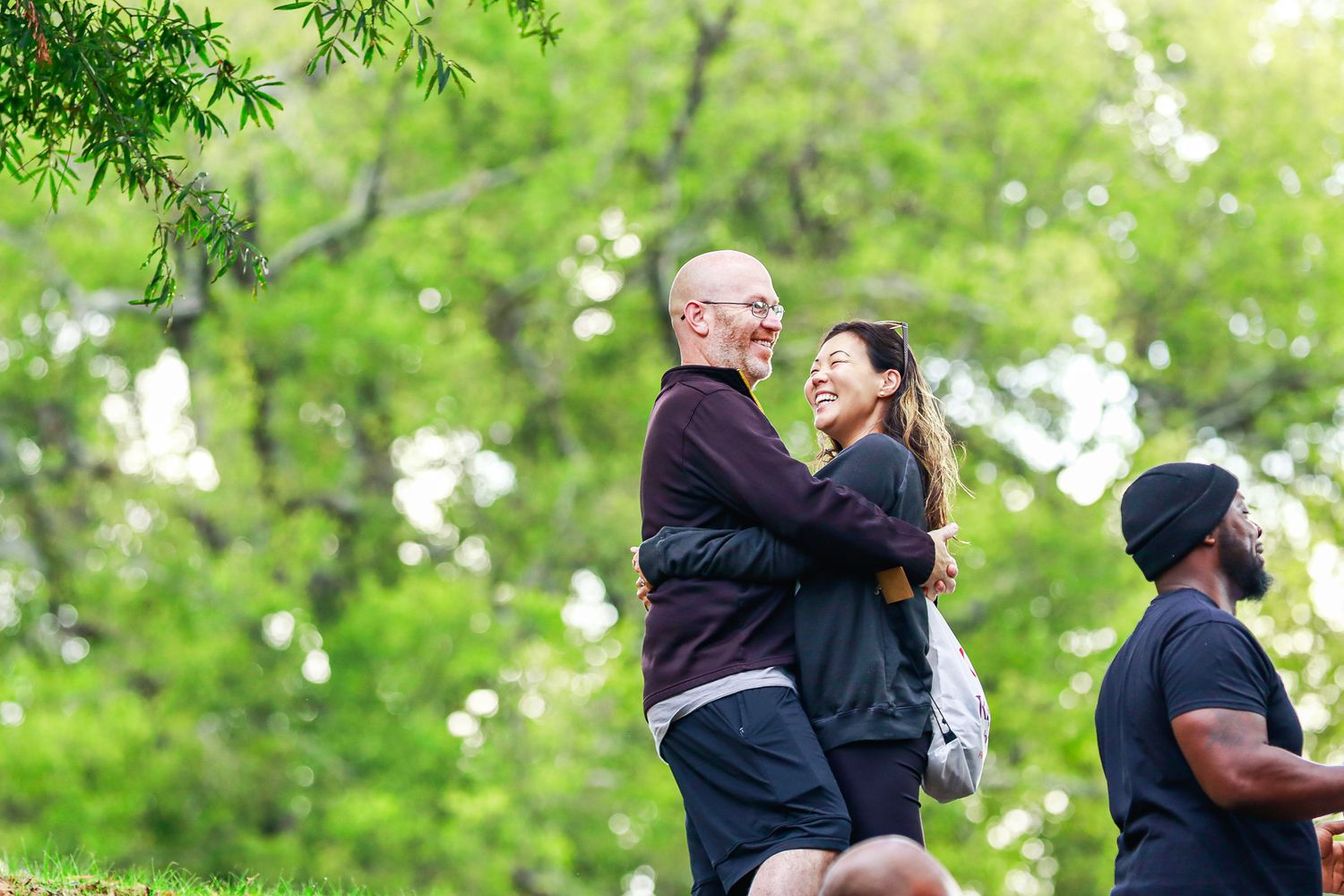 Couple dancing together outdoors in a park with lush green trees and natural lighting in the background.