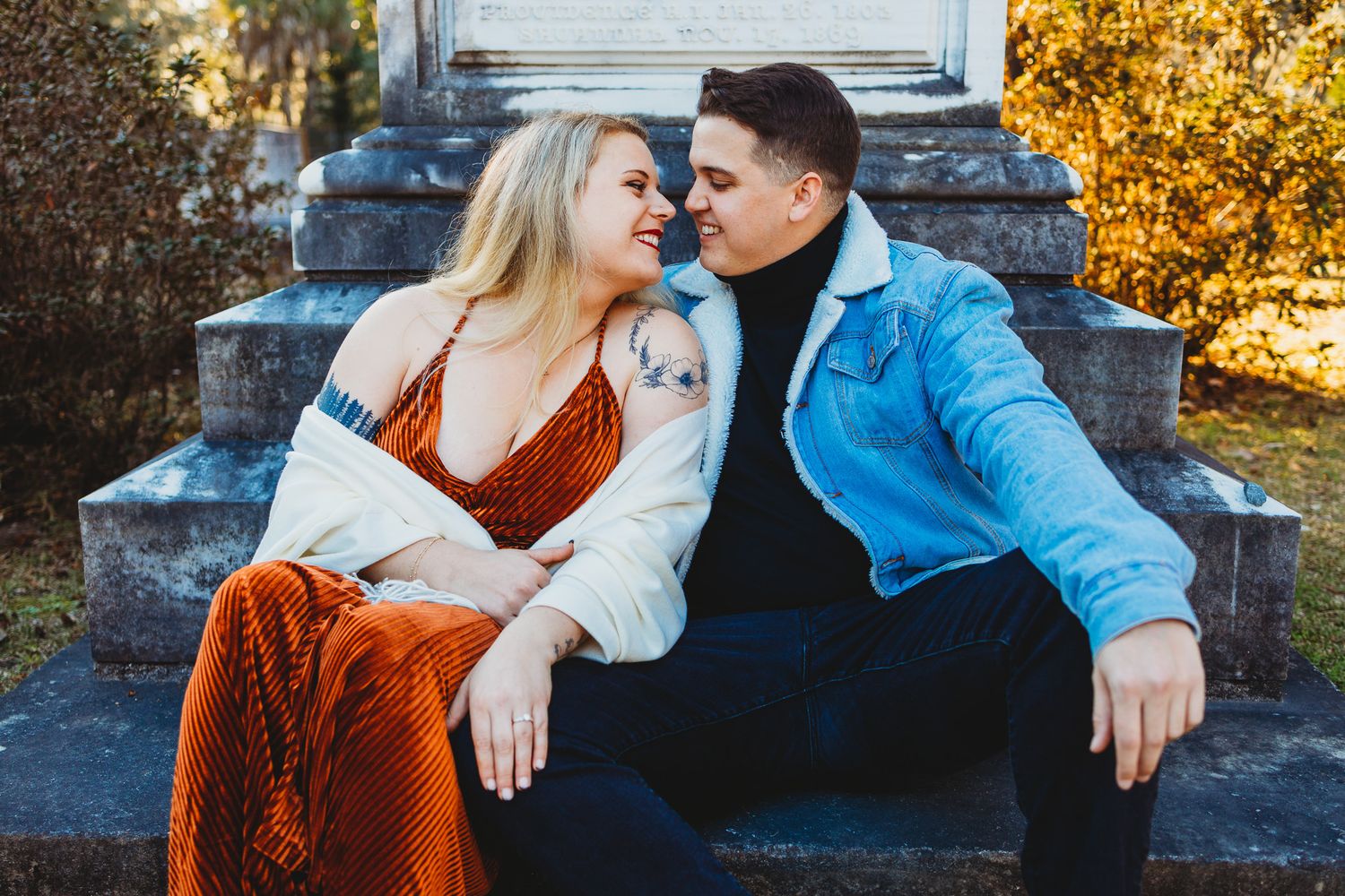 A couple shares intimate moments in a fall setting with golden foliage and stone steps in the background.