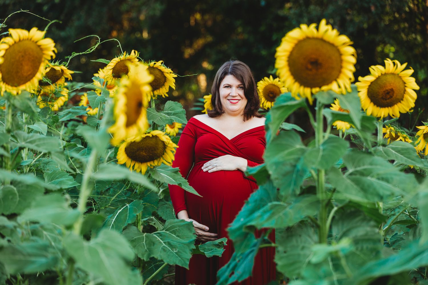 Woman in red dress poses in vibrant sunflower field during golden hour photoshoot.