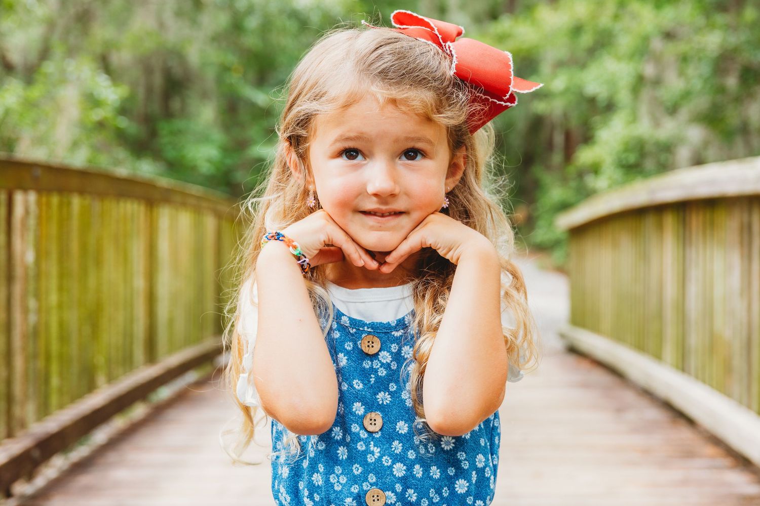 Young girl in blue dress and red bow playing on wooden boardwalk.