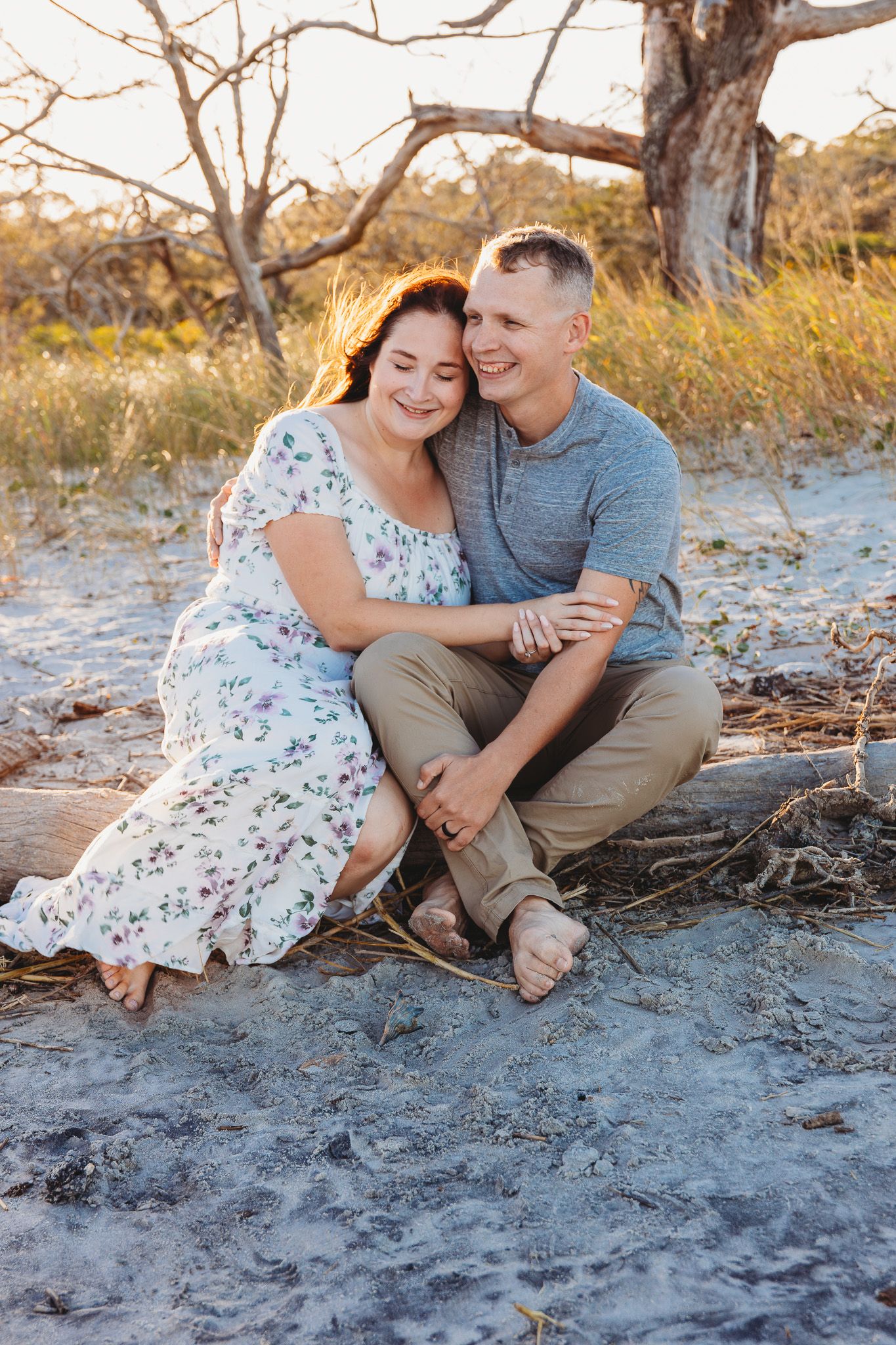 A couple shares a romantic moment sitting together on a sandy beach at sunset.