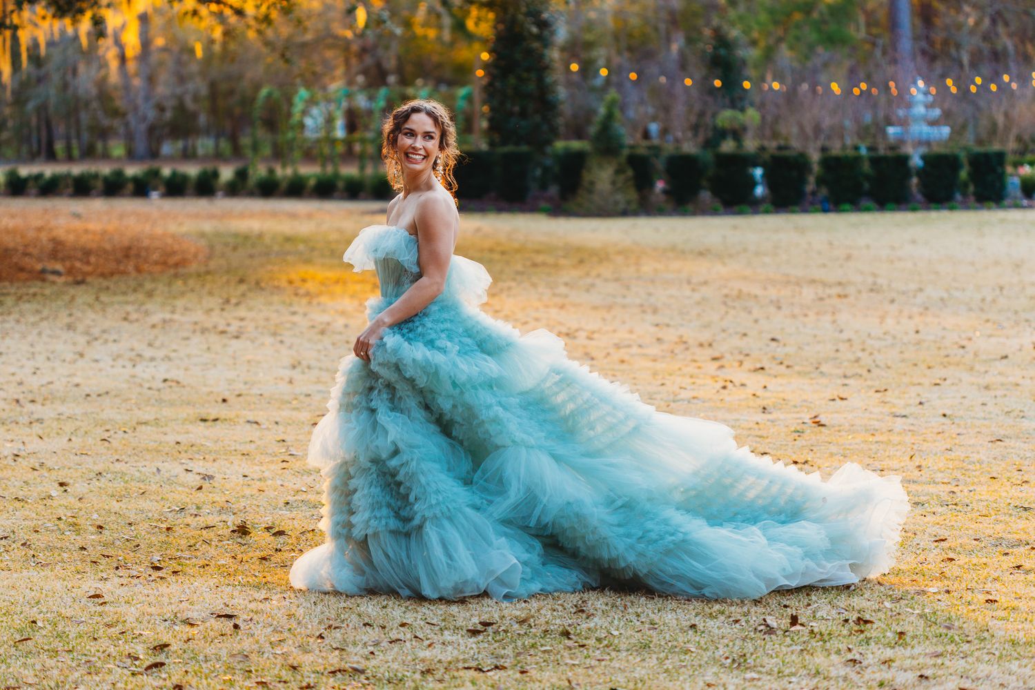 A flowing turquoise gown with ruffled layers sweeps across autumn leaves in a dreamy outdoor portrait session.