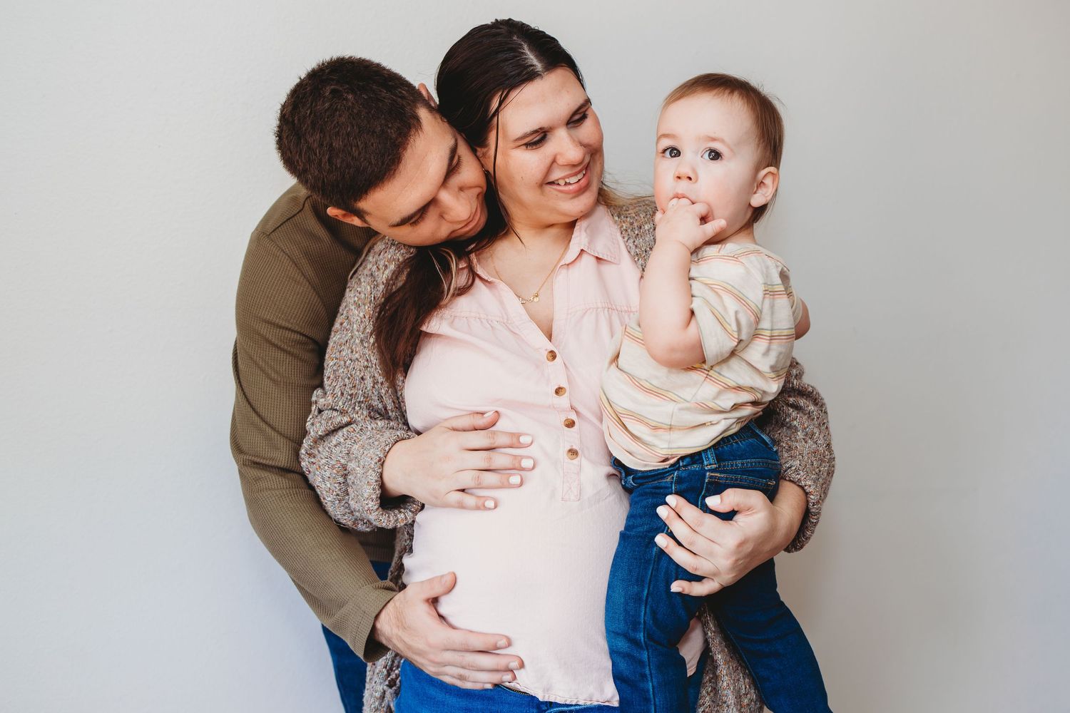 Family portrait series showing tender moments with a baby against a light gray background.