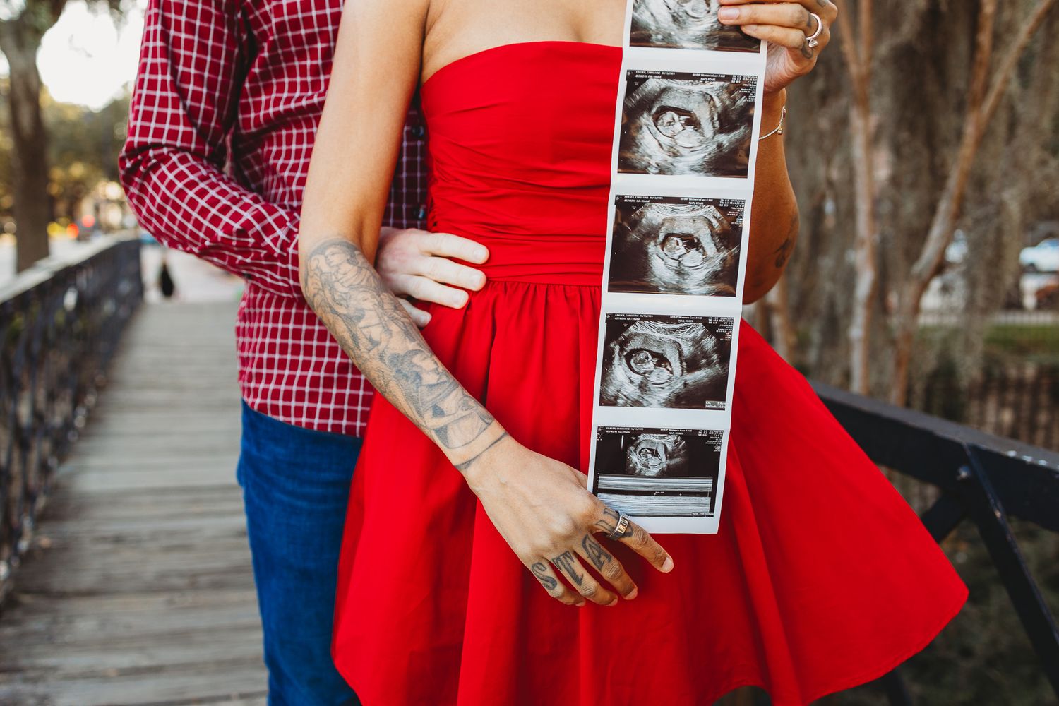 Couple holds ultrasound photos while wearing red and plaid clothing outdoors.