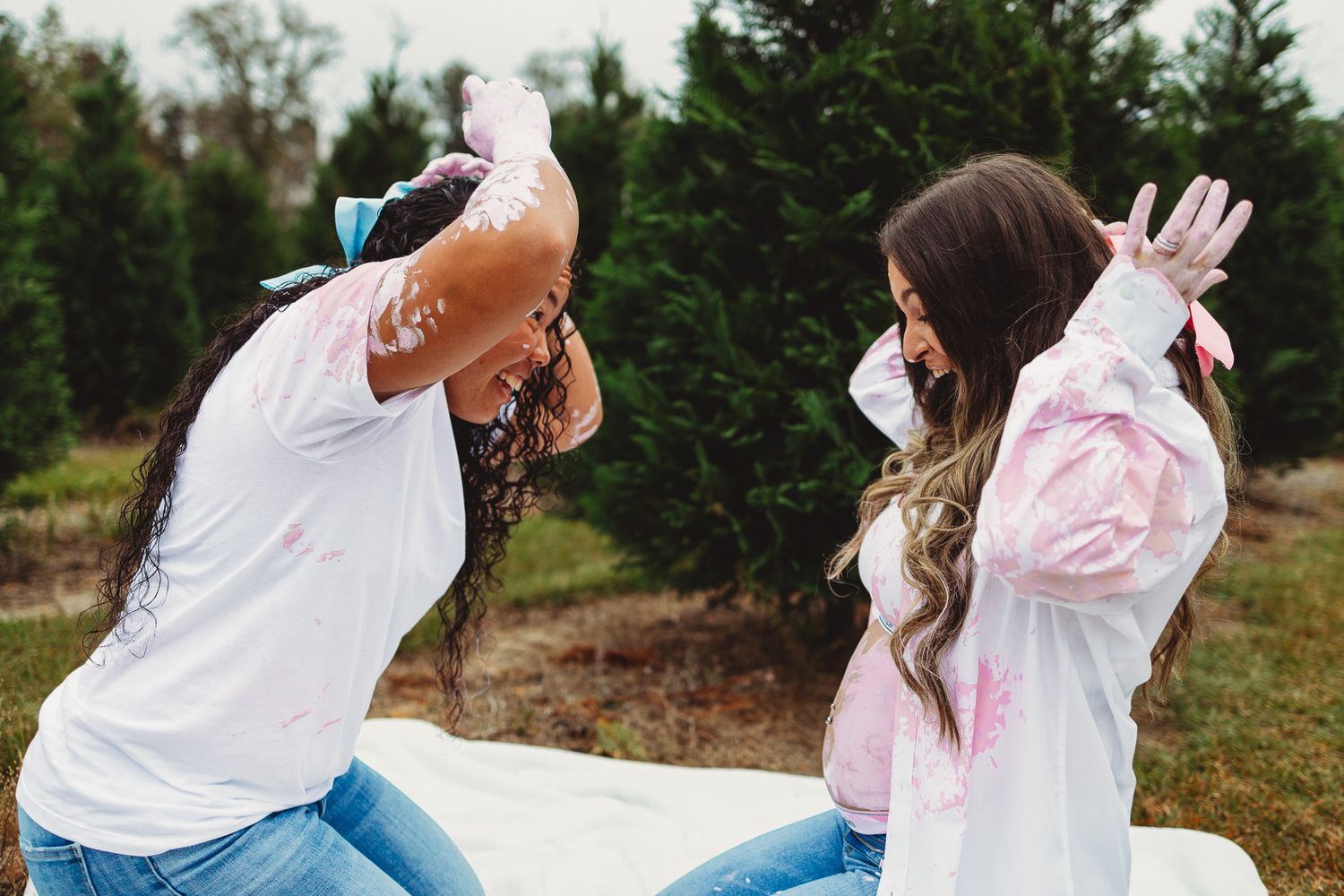 A group of people wearing white shirts and jeans throw pink powder into the air during a festive outdoor celebration.
