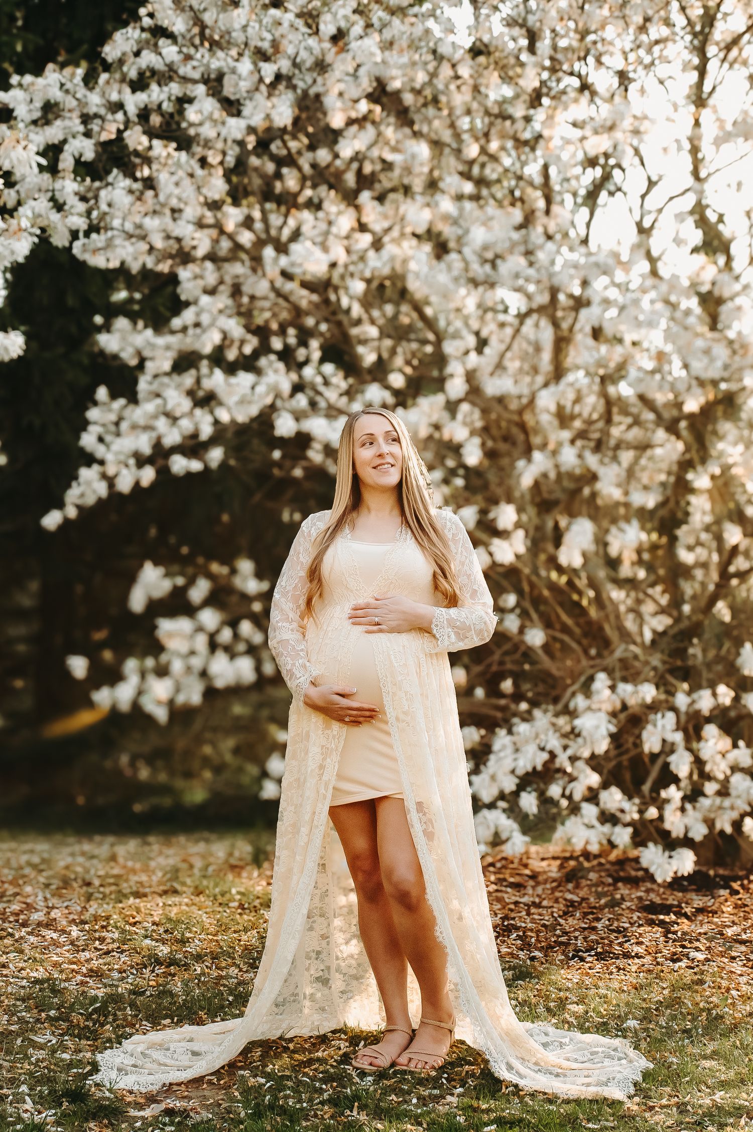 Ethereal maternity photo with white cherry blossoms and flowing lace dress.