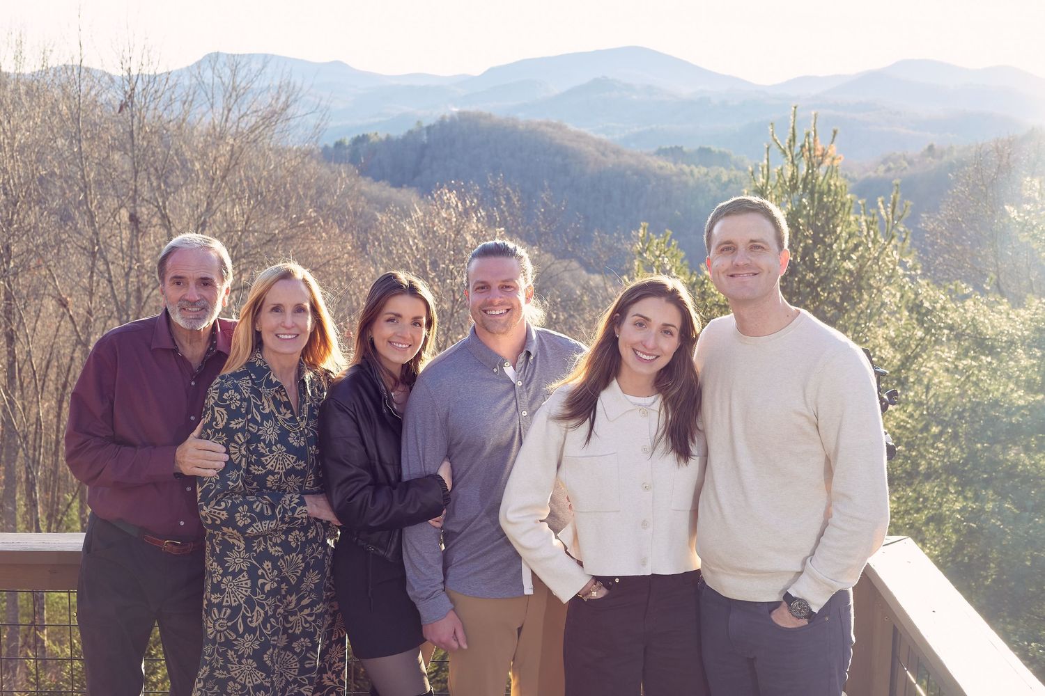 A group stands together on a deck with scenic mountain views in the background on a sunny day.