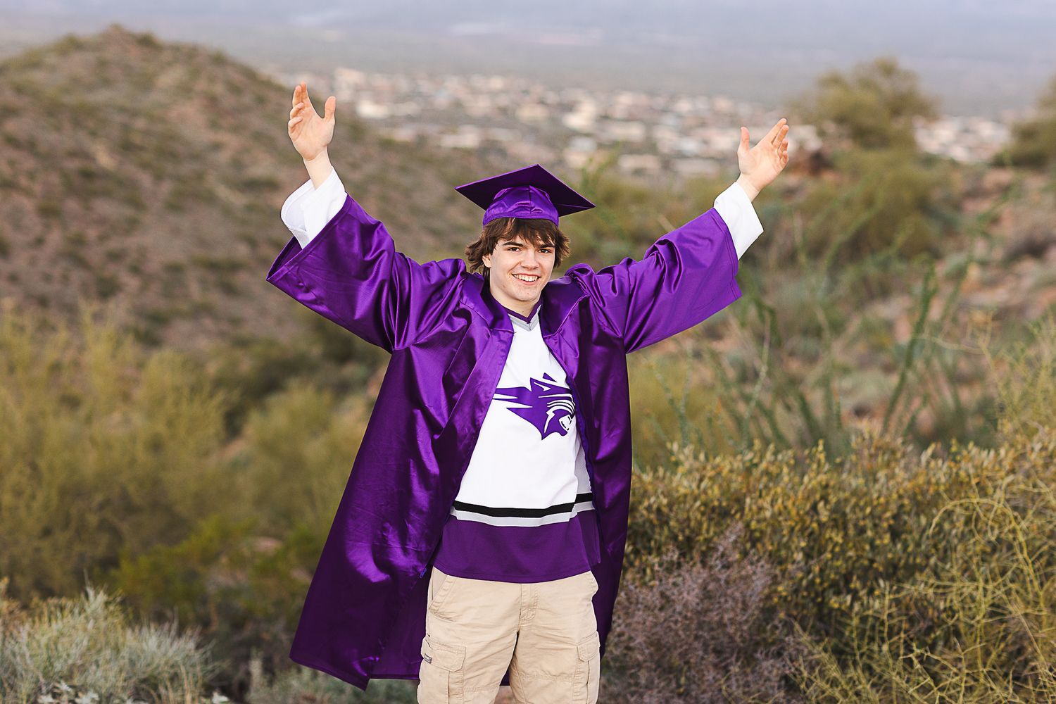 A person in a purple jacket and white shirt poses joyfully against a scenic mountain landscape background.