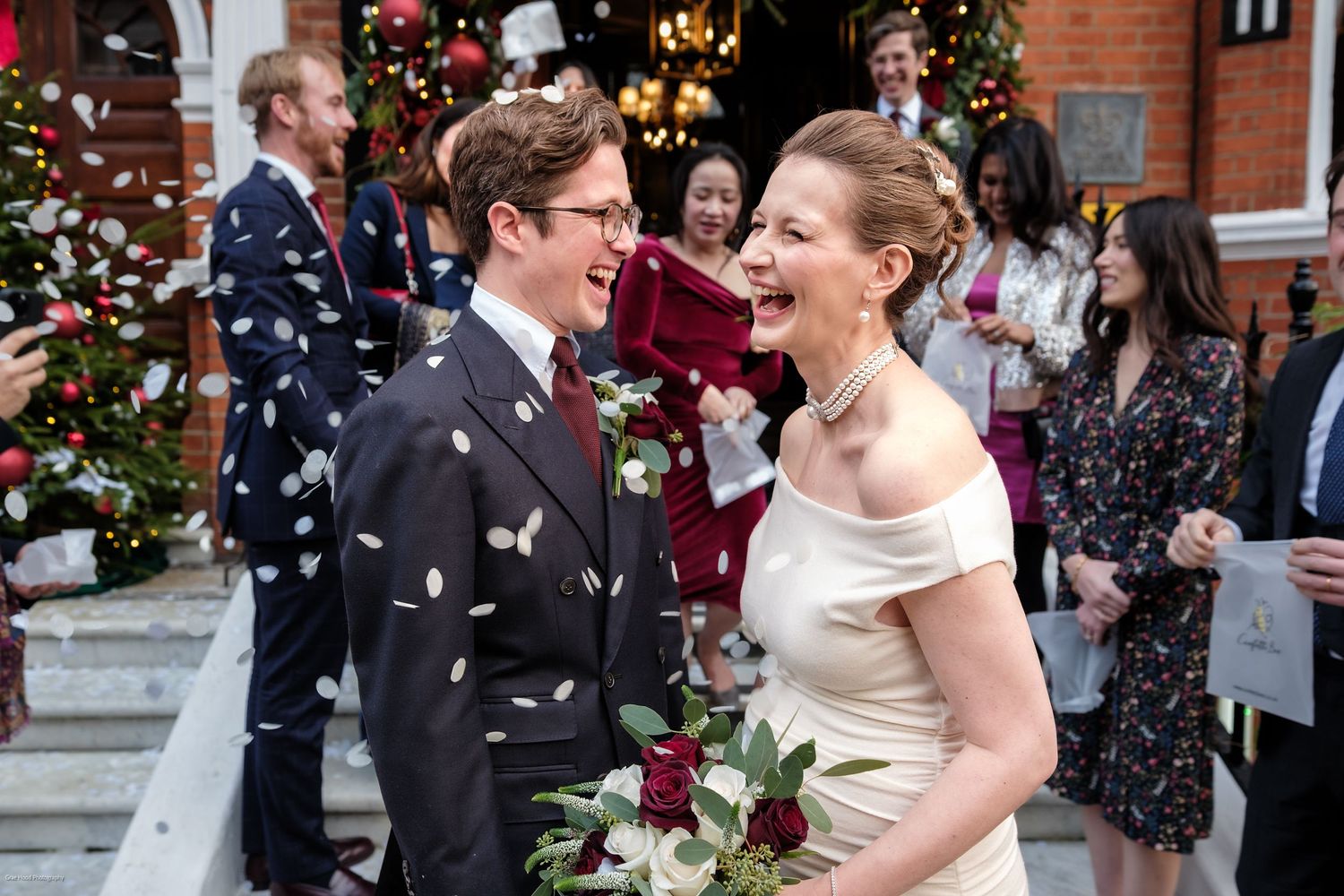 A joyful couple shares a romantic moment during their winter wedding celebration with confetti and Christmas decorations.
