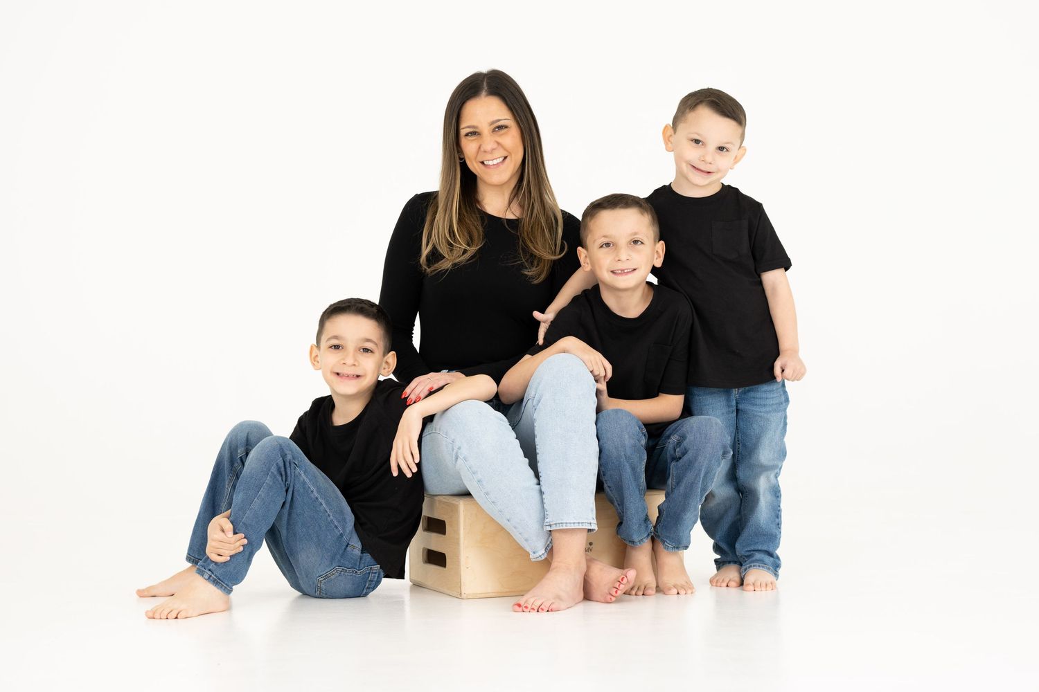 Family portrait of mother and three sons wearing coordinated black and denim outfits on white background.