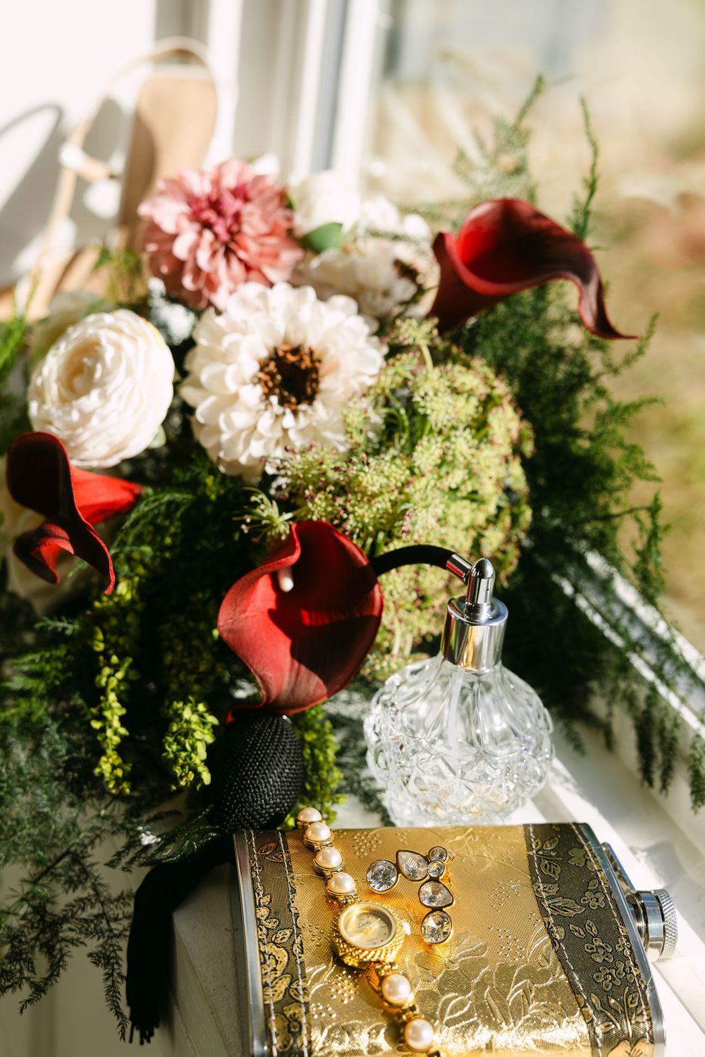 Elegant wedding details featuring red and white flowers with greenery arranged beside vintage gold decor and crystal pieces.