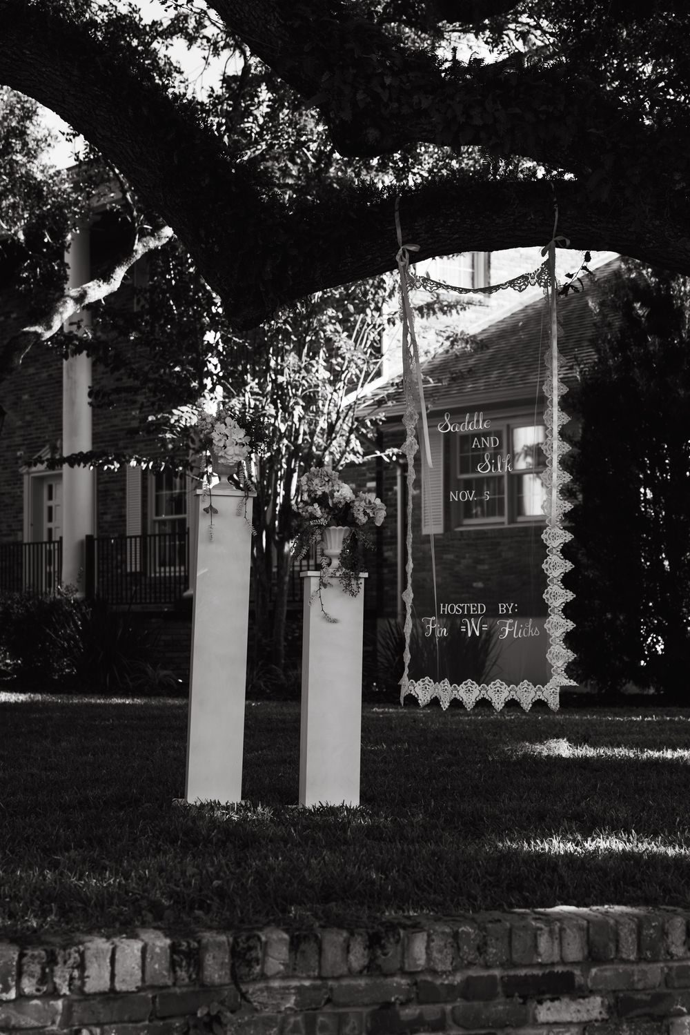 Black and white photo showing stone pillars and steps leading to a building entrance in a shaded garden setting.