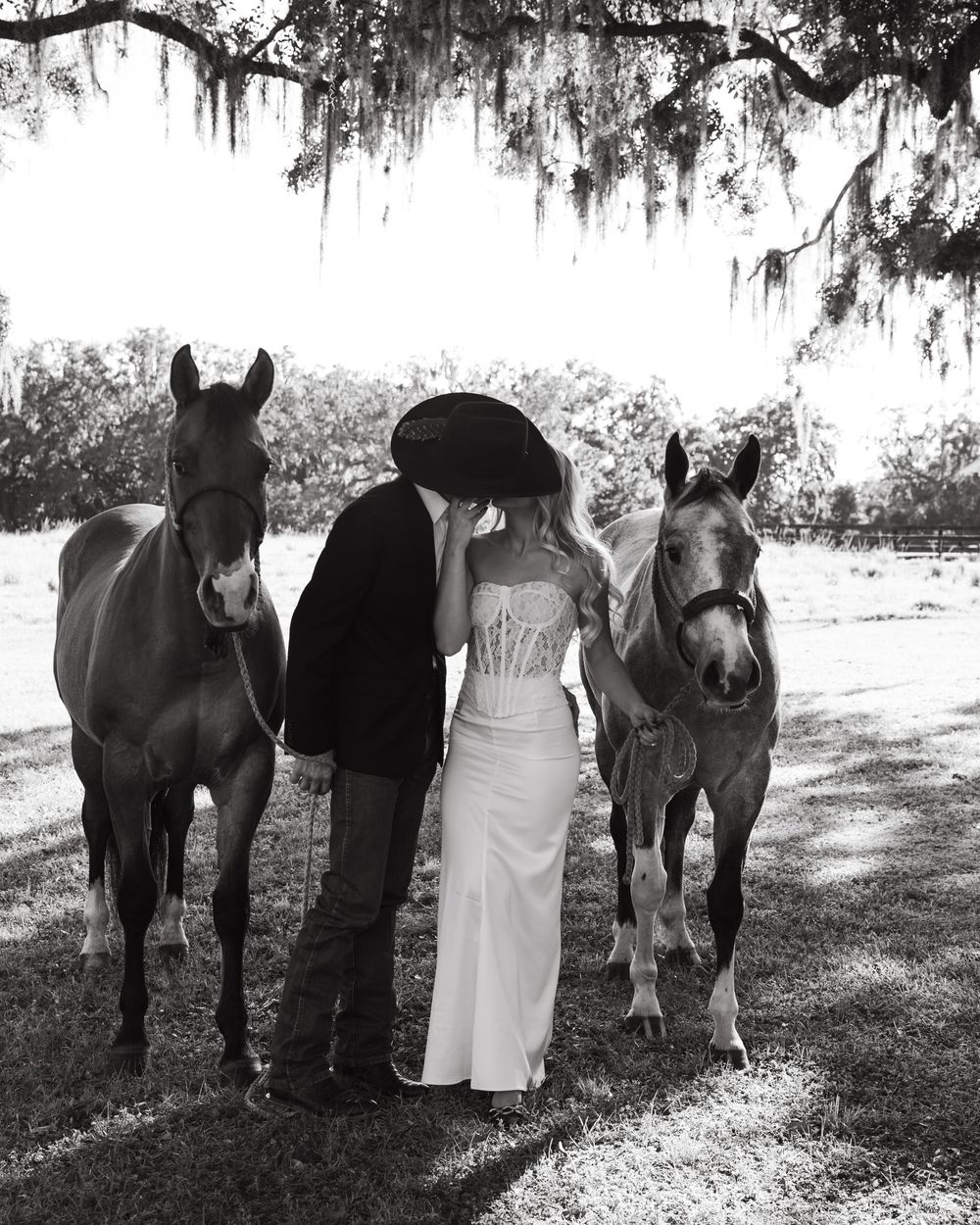 A romantic couple poses with their horses under Spanish moss draped trees in a series of black and white photos.