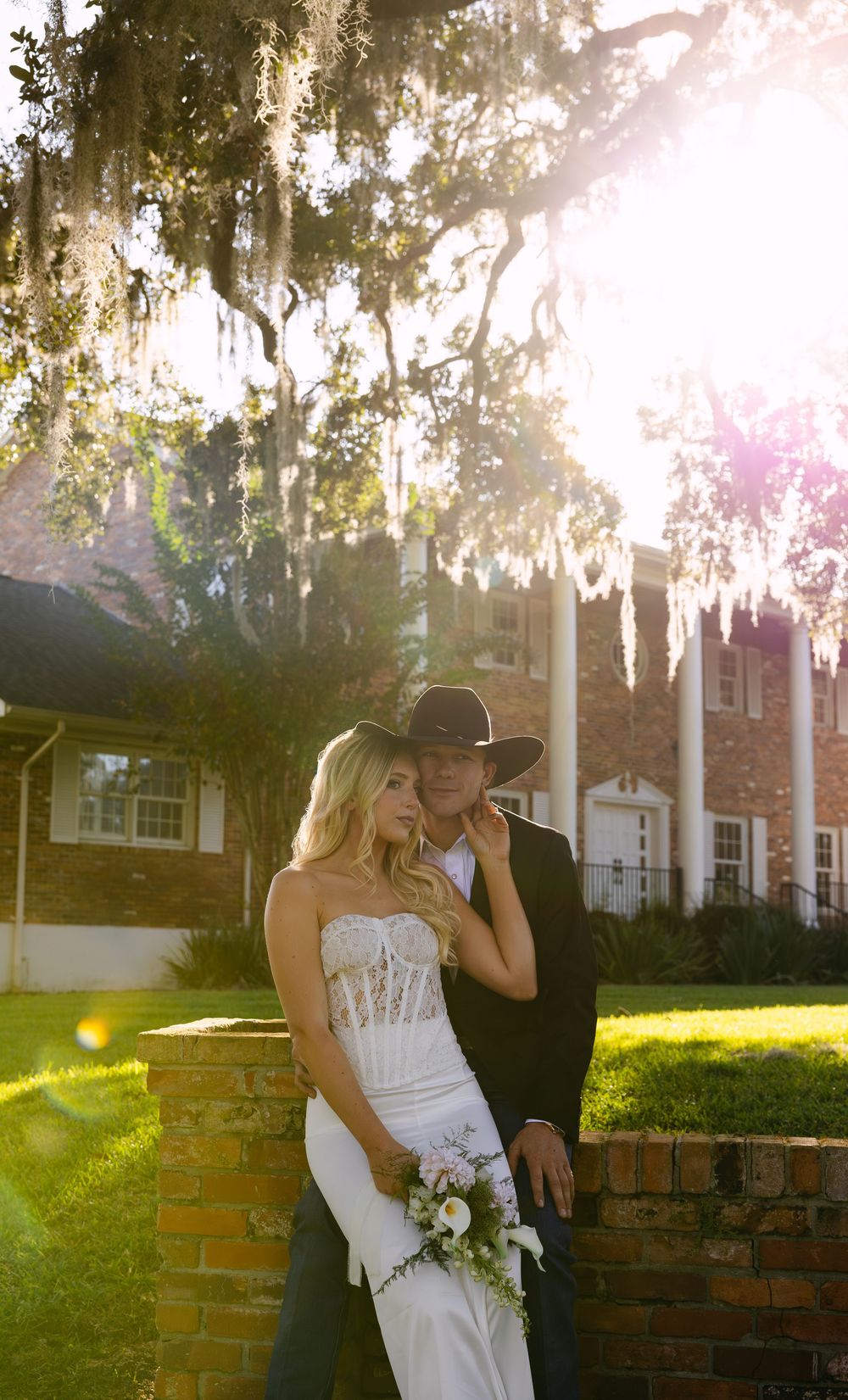 A romantic wedding photo at sunset with Spanish moss hanging from trees and a stately home in the background.