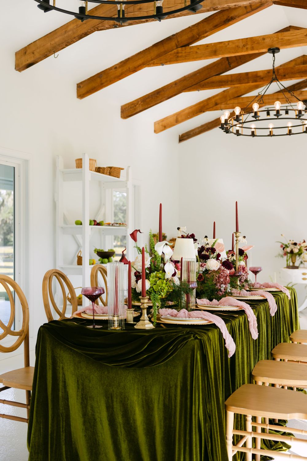 Elegant wedding reception table setup with dark green tablecloths and floral centerpieces under rustic wooden beams.
