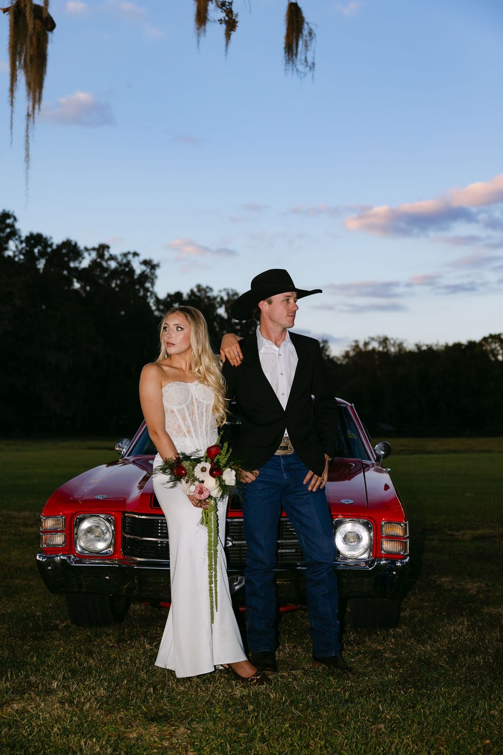 A vintage red car serves as a backdrop for an evening countryside photoshoot at sunset.