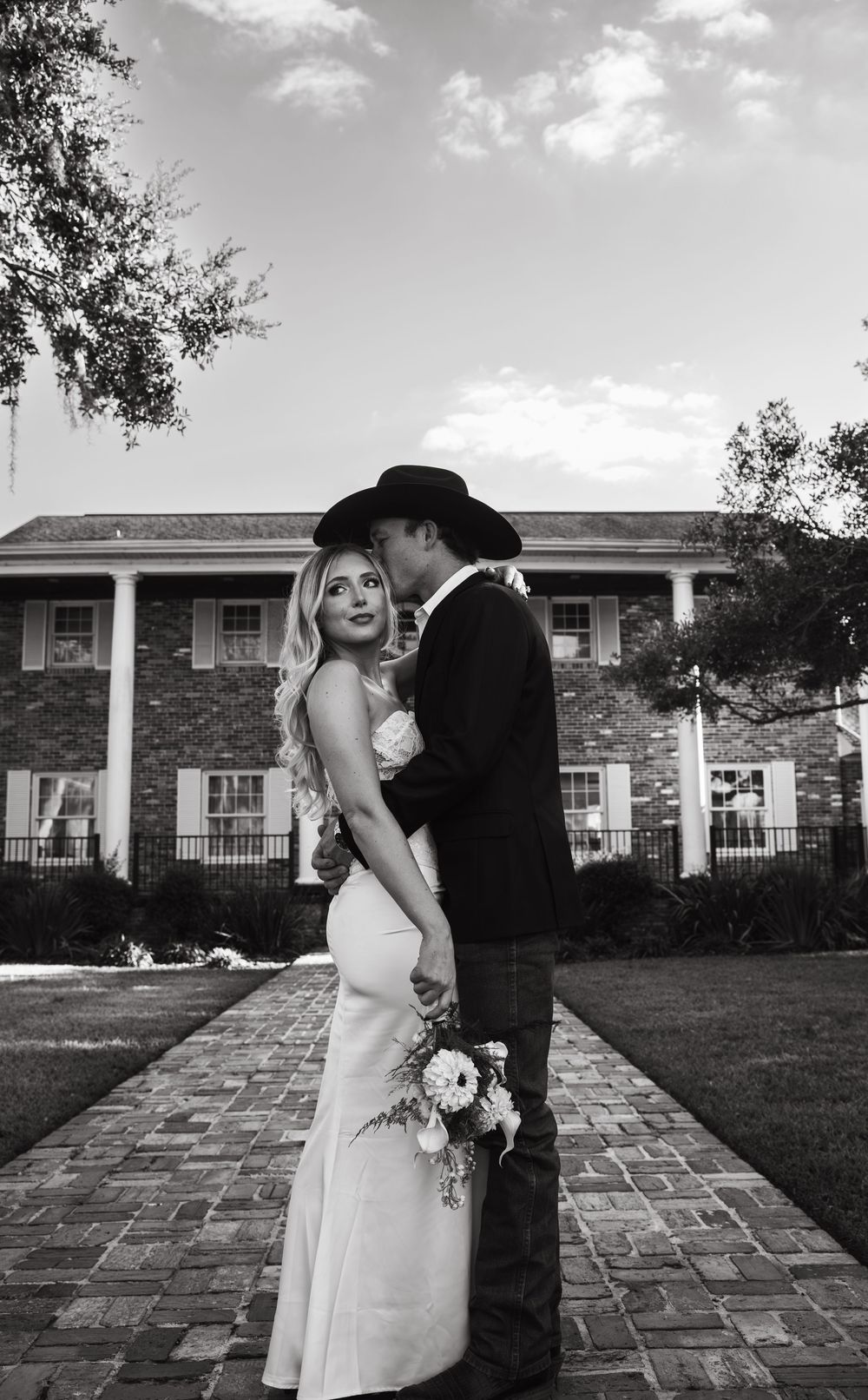 A black and white wedding portrait in front of a brick colonial style building with white columns.