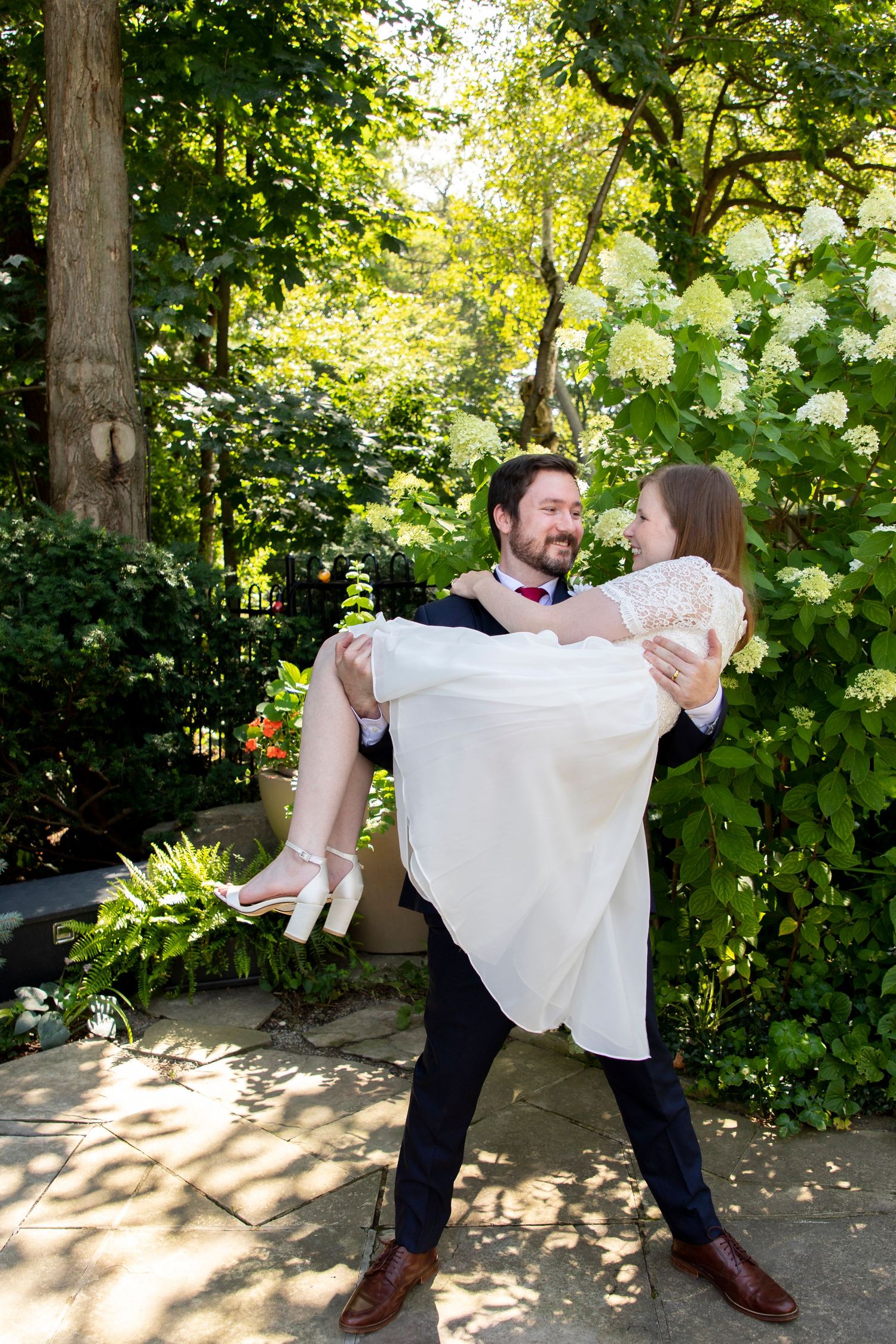 A groom carrying his bride in front of a beautiful hydrangea garden