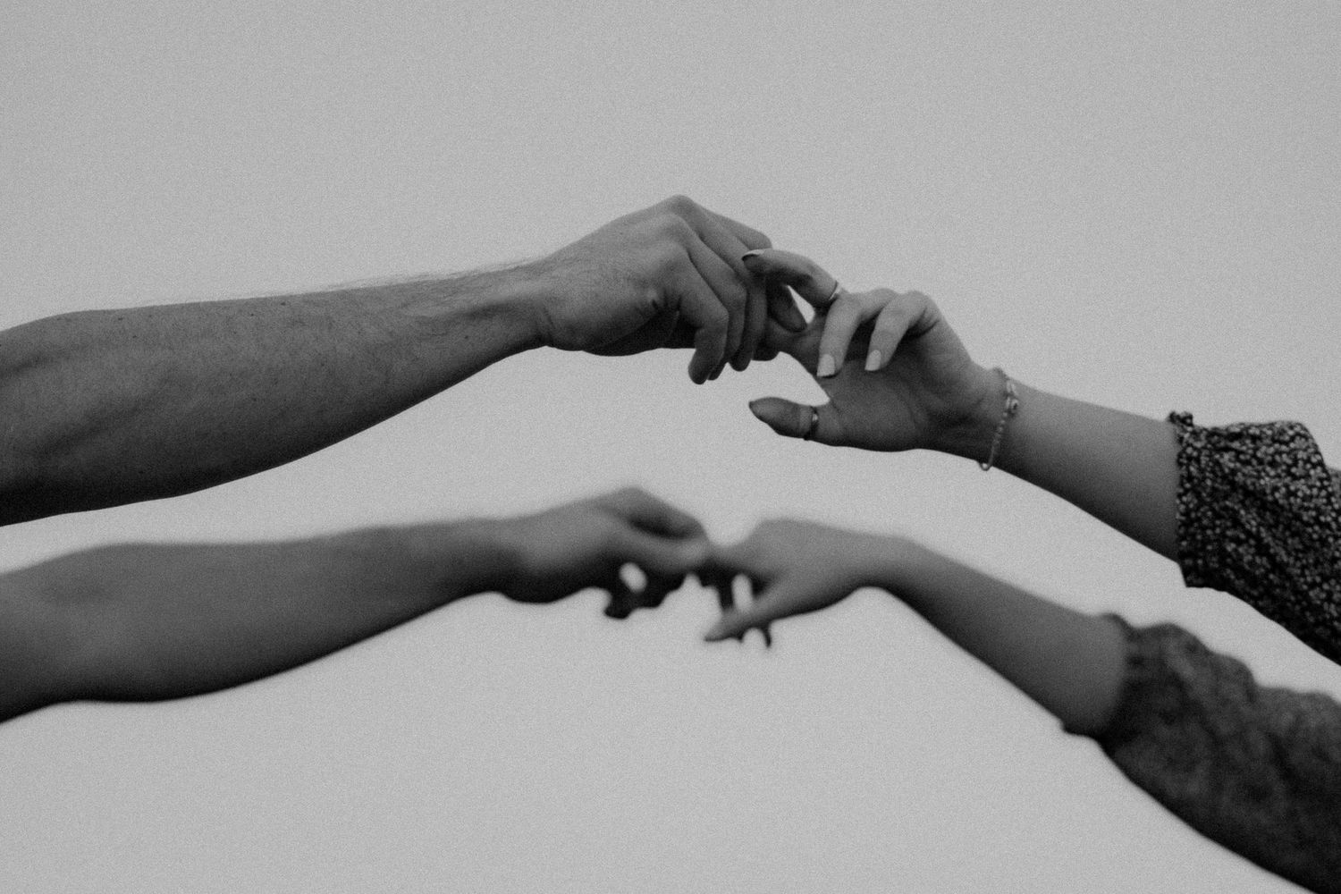 Two hands reach out to touch each other in a tender black and white photograph.