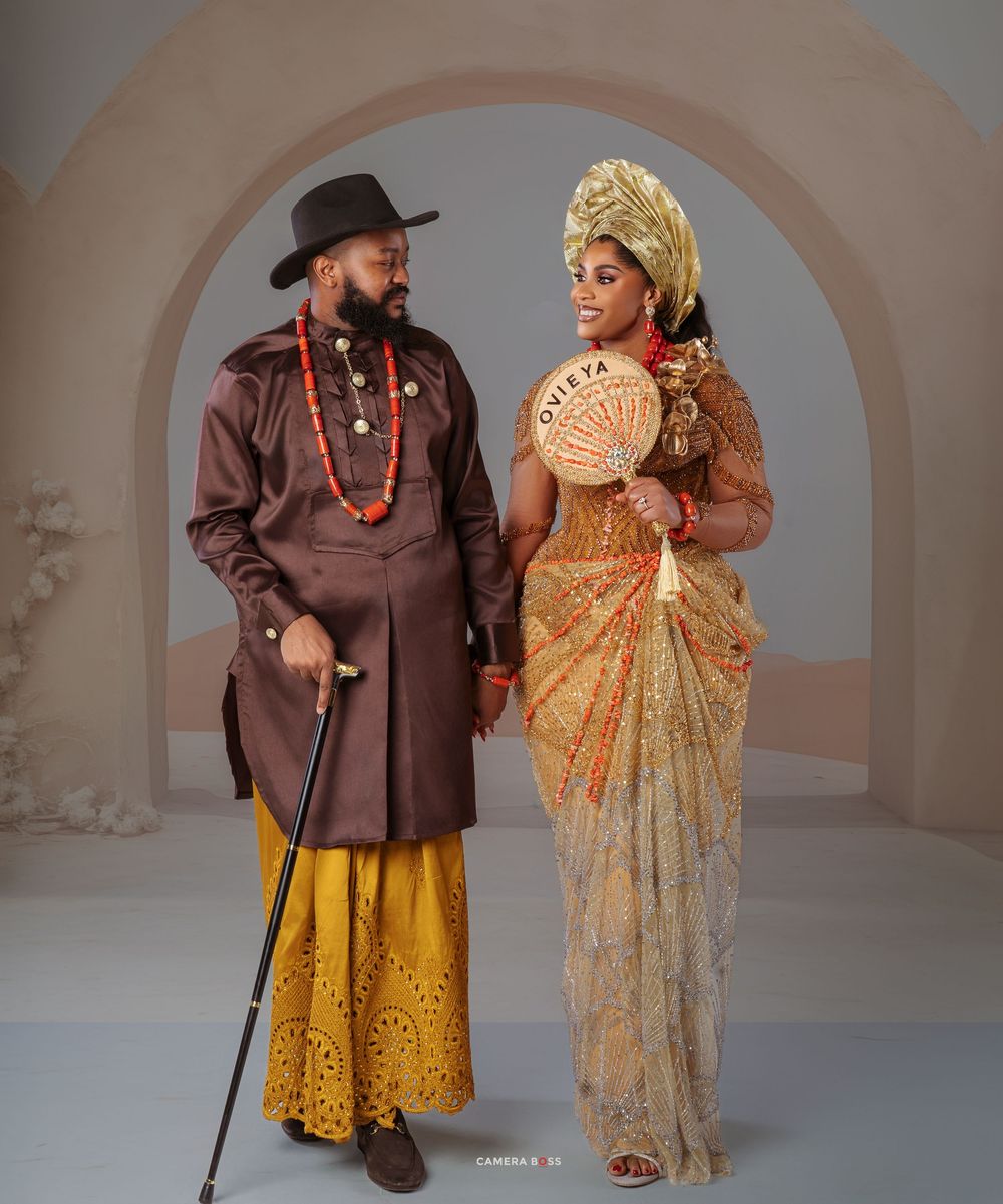 Traditional Nigerian wedding attire featuring brown and gold formal wear with cultural accessories and elegant styling.