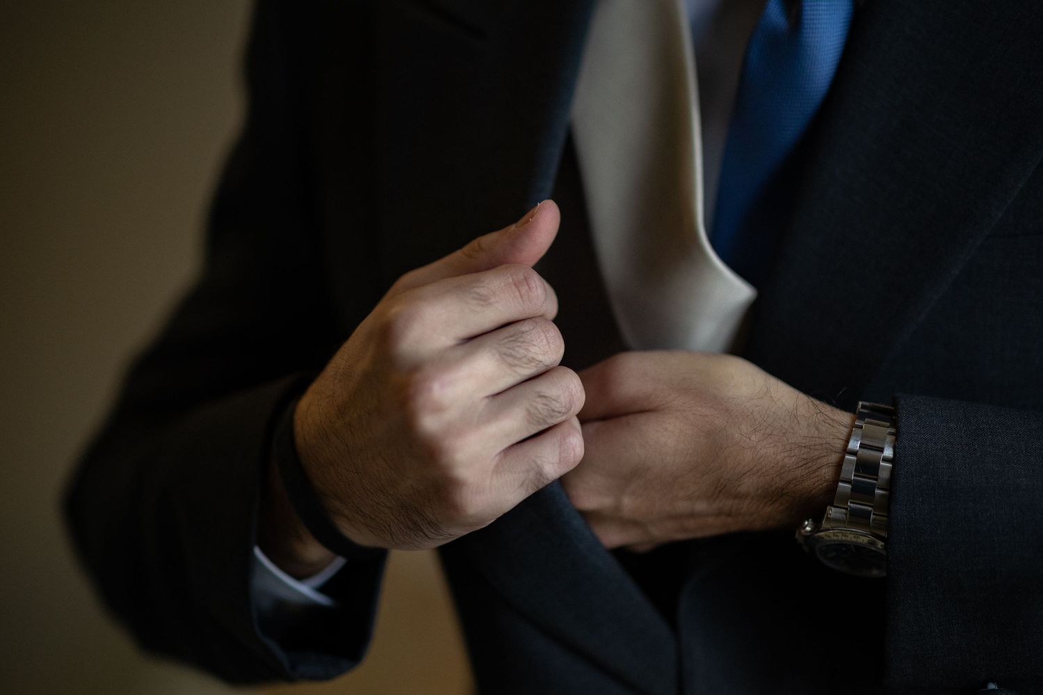 Close-up view of hands adjusting a dark suit jacket sleeve with a watch visible.