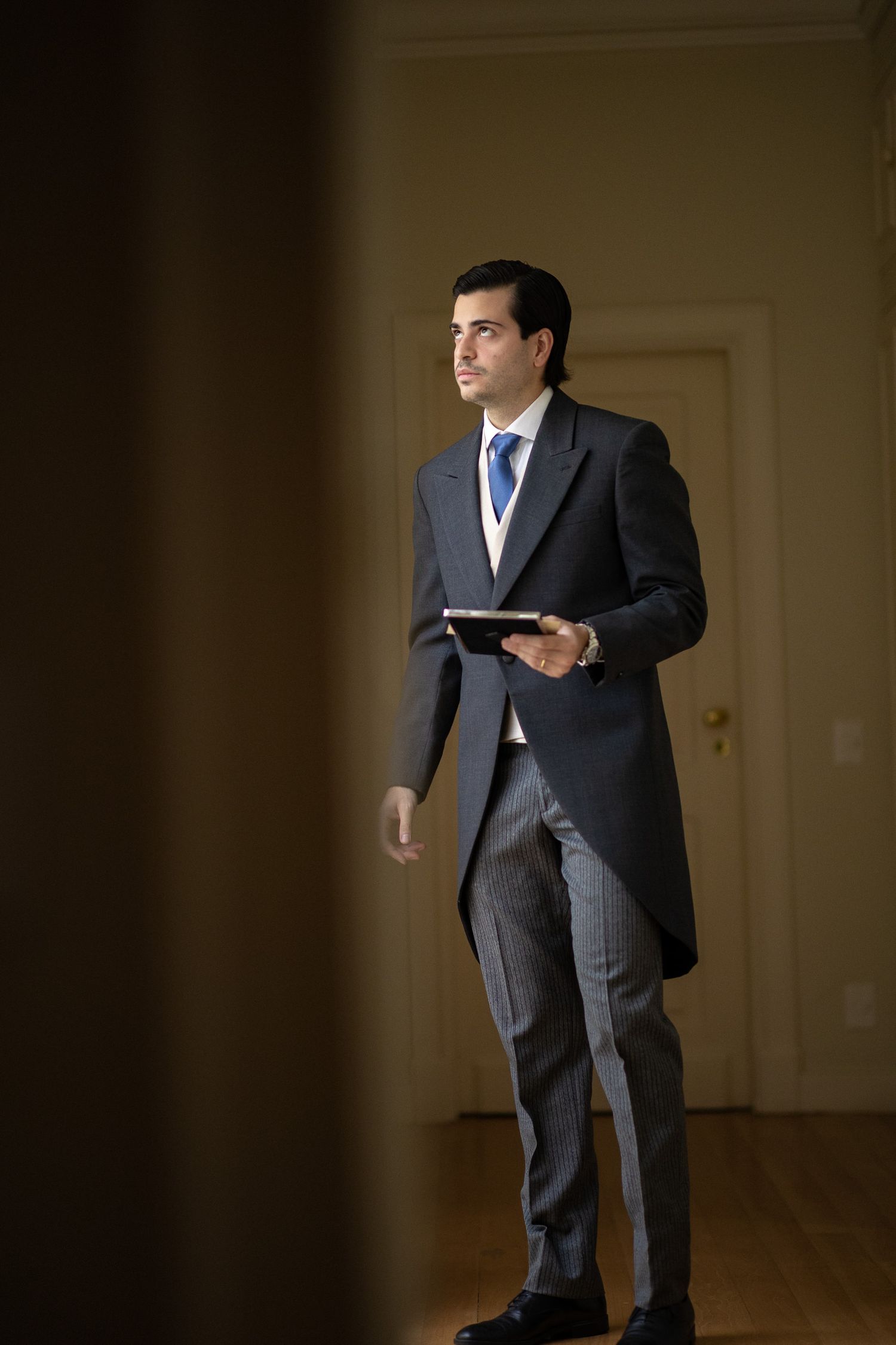 Professional in a dark suit stands in various dynamic poses while holding a tablet device in a dimly lit room.